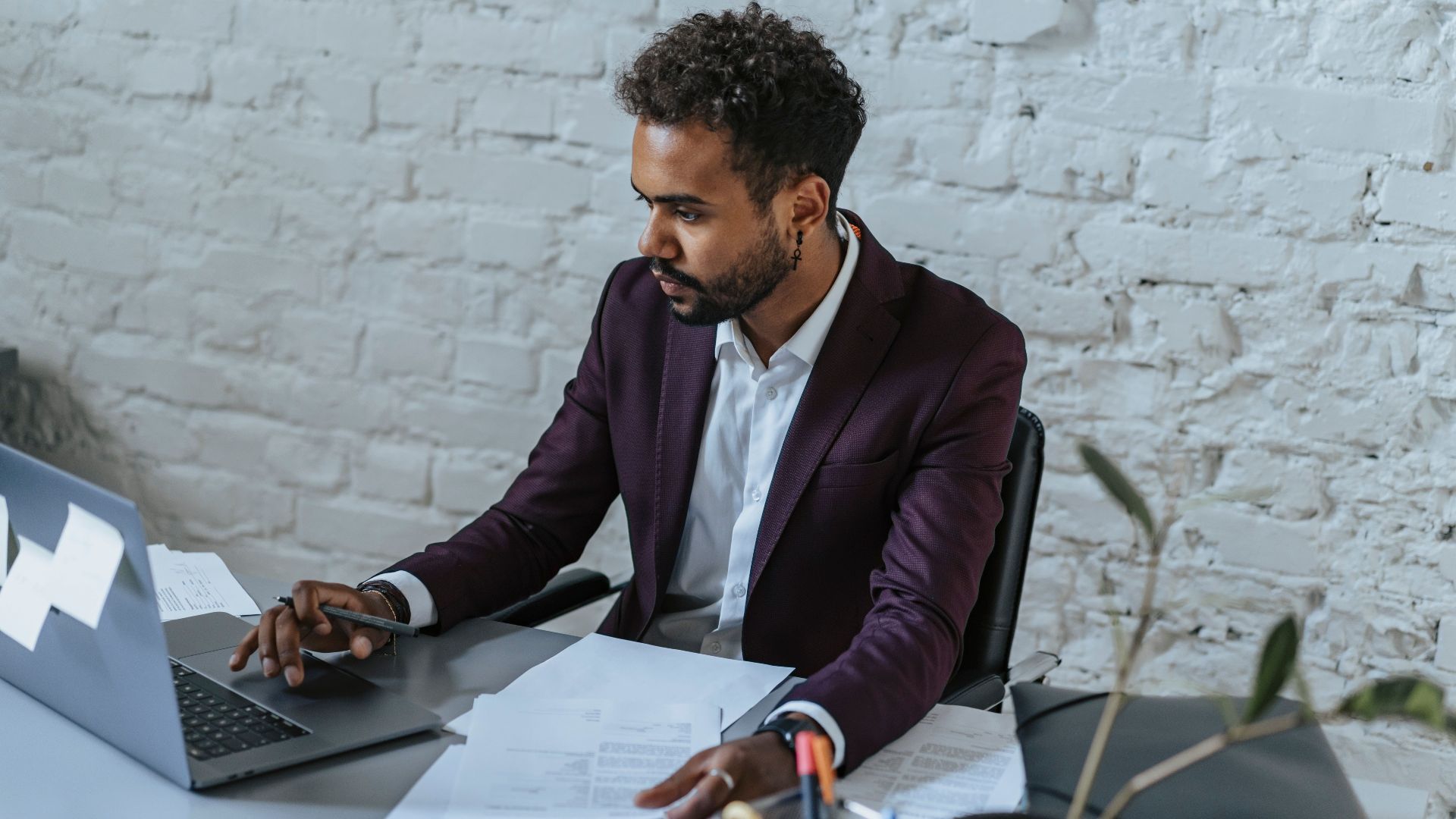 Professional man with curly hair working on a laptop in a stylish office setting.