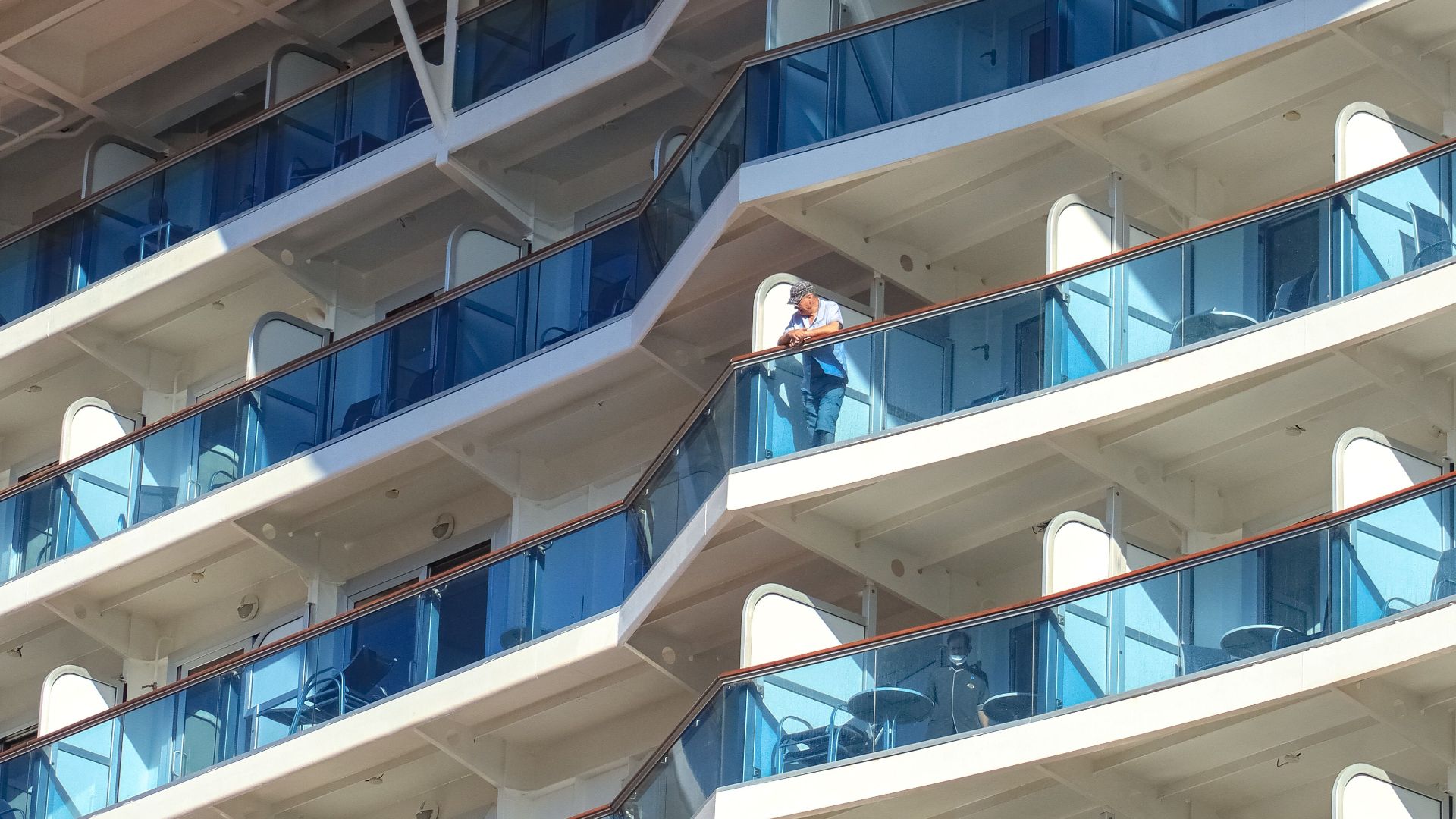Detailed view of a modern cruise ship's balcony-filled exterior under a bright blue sky.
