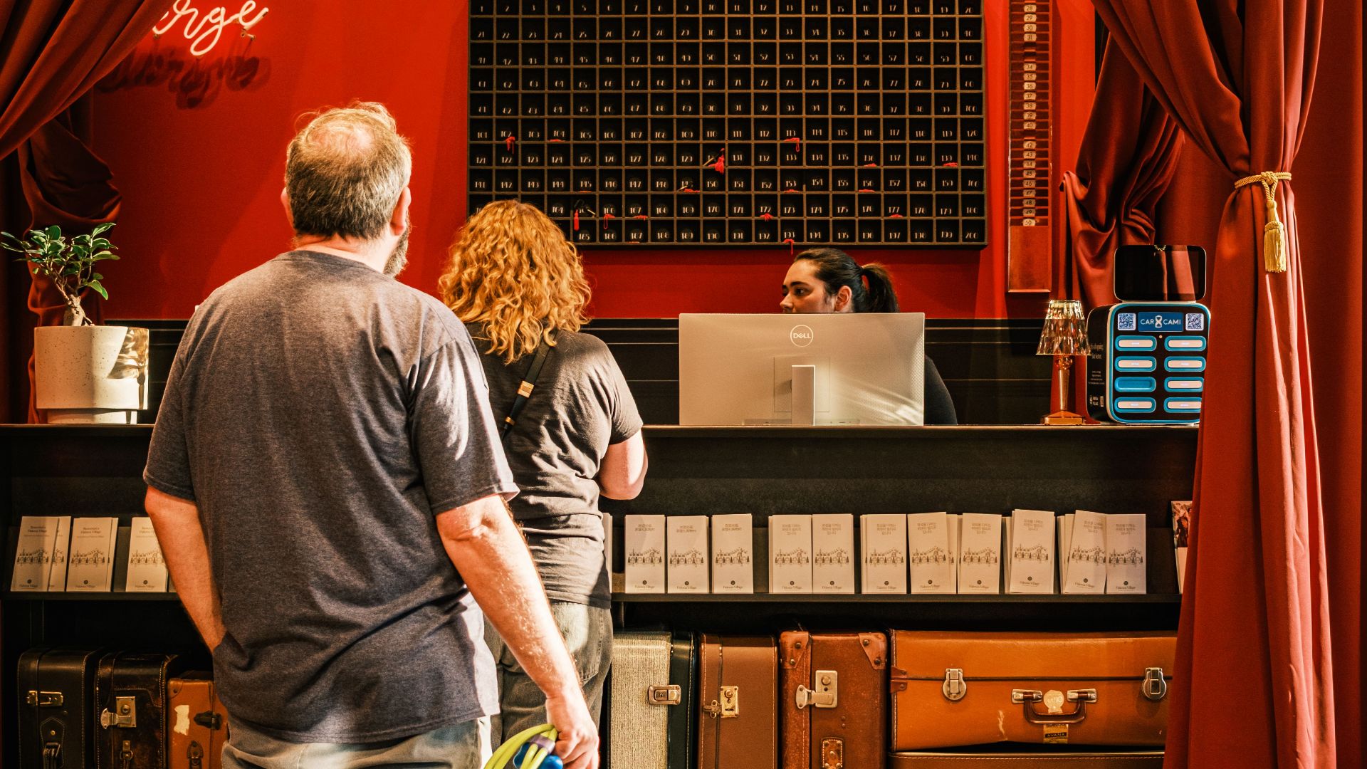 A couple with a dog checks in at a stylish, vintage hotel front desk.