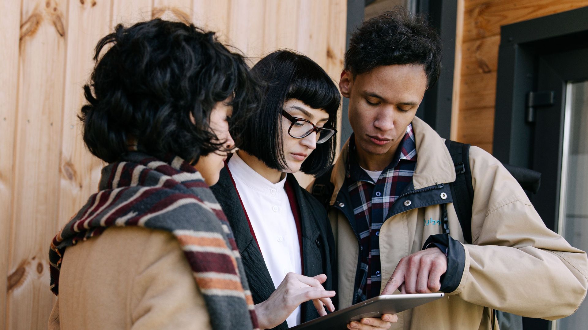 Three adults collaborating using a digital tablet against a wooden wall, possibly real estate agents.