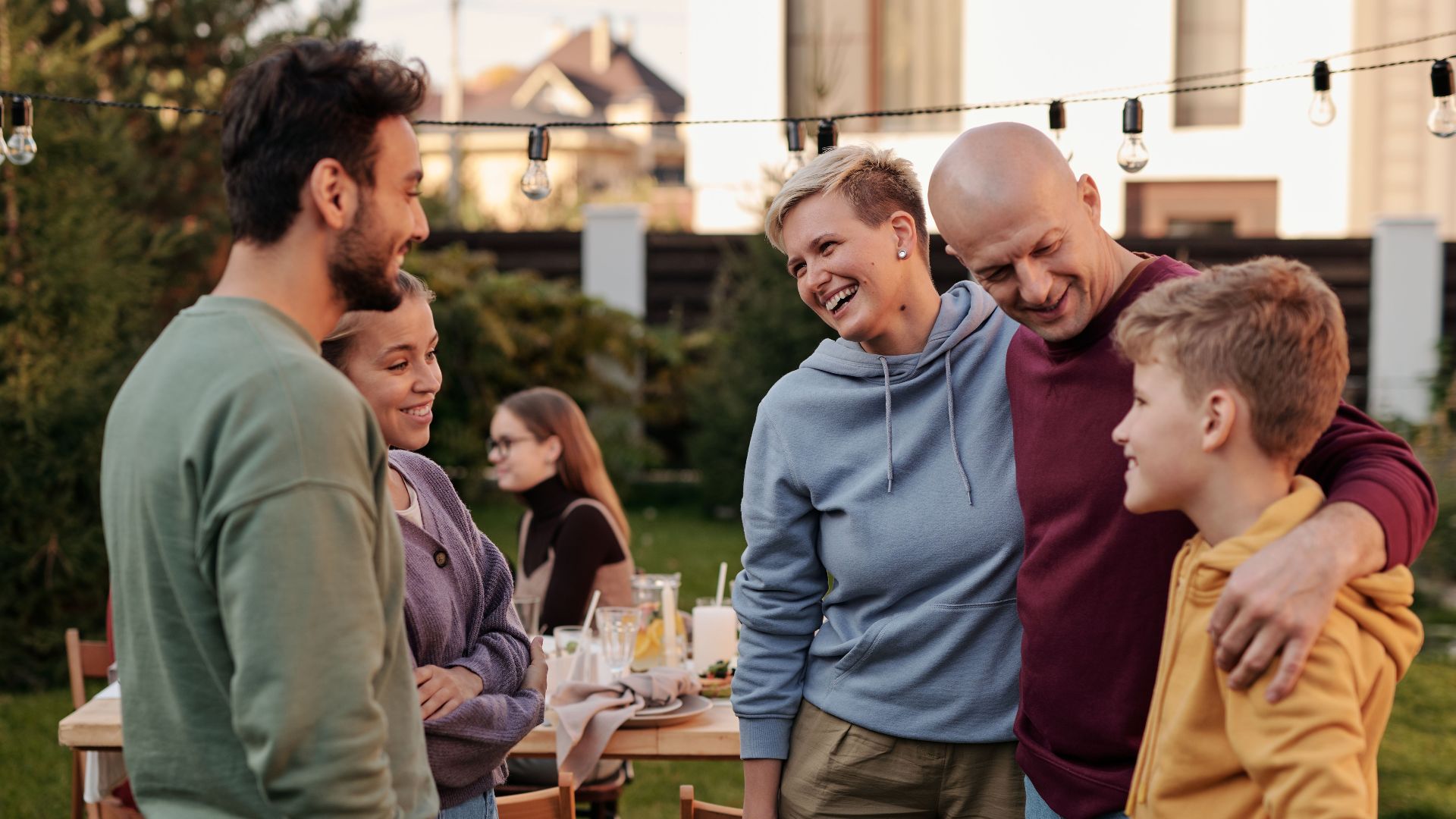 Happy family in casual clothes laughing and having picnic in backyard with string of light bulbs in daytime
