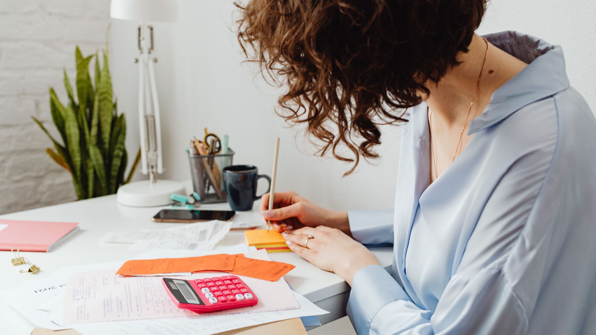 Woman writing with calculator on desk, managing finances indoors.