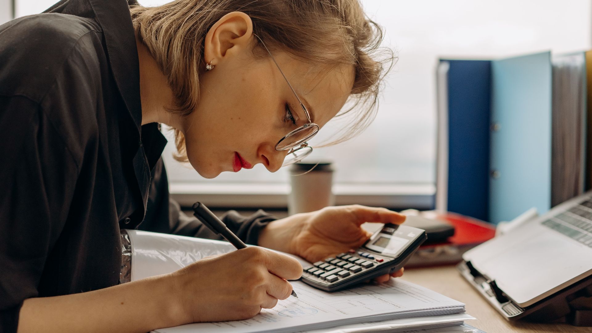 Young woman diligently working on accounting with a calculator and documents. Perfect for business and finance themes.
