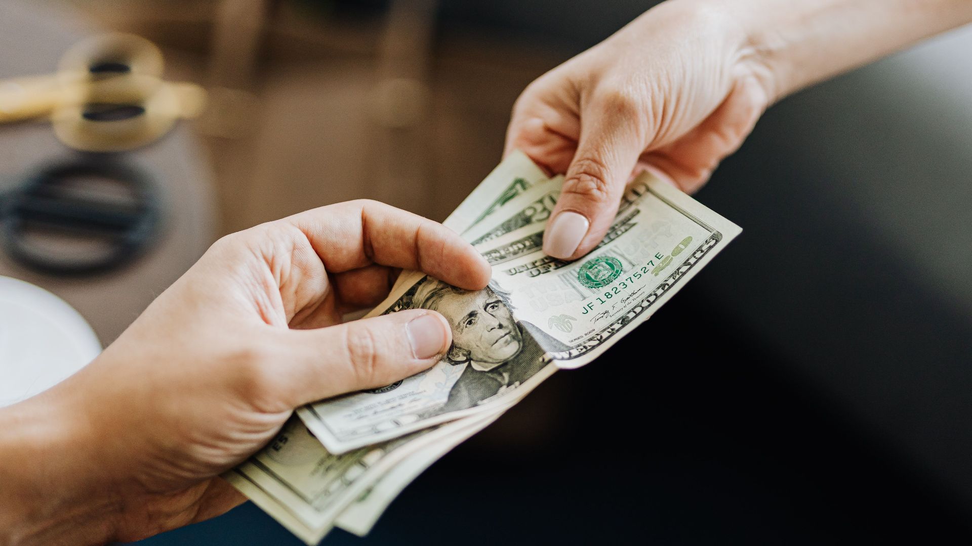 A close-up image of hands exchanging US dollar bills, symbolizing financial transaction or payment.