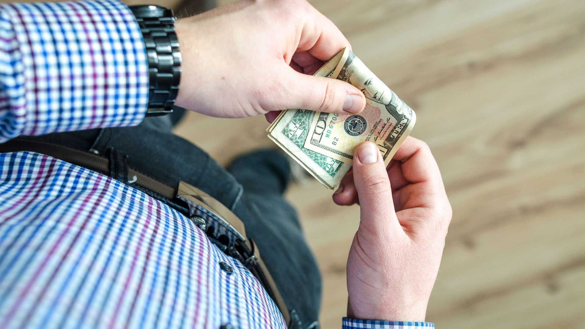Close-up view of a man in casual clothes holding US dollar bills in his hands.