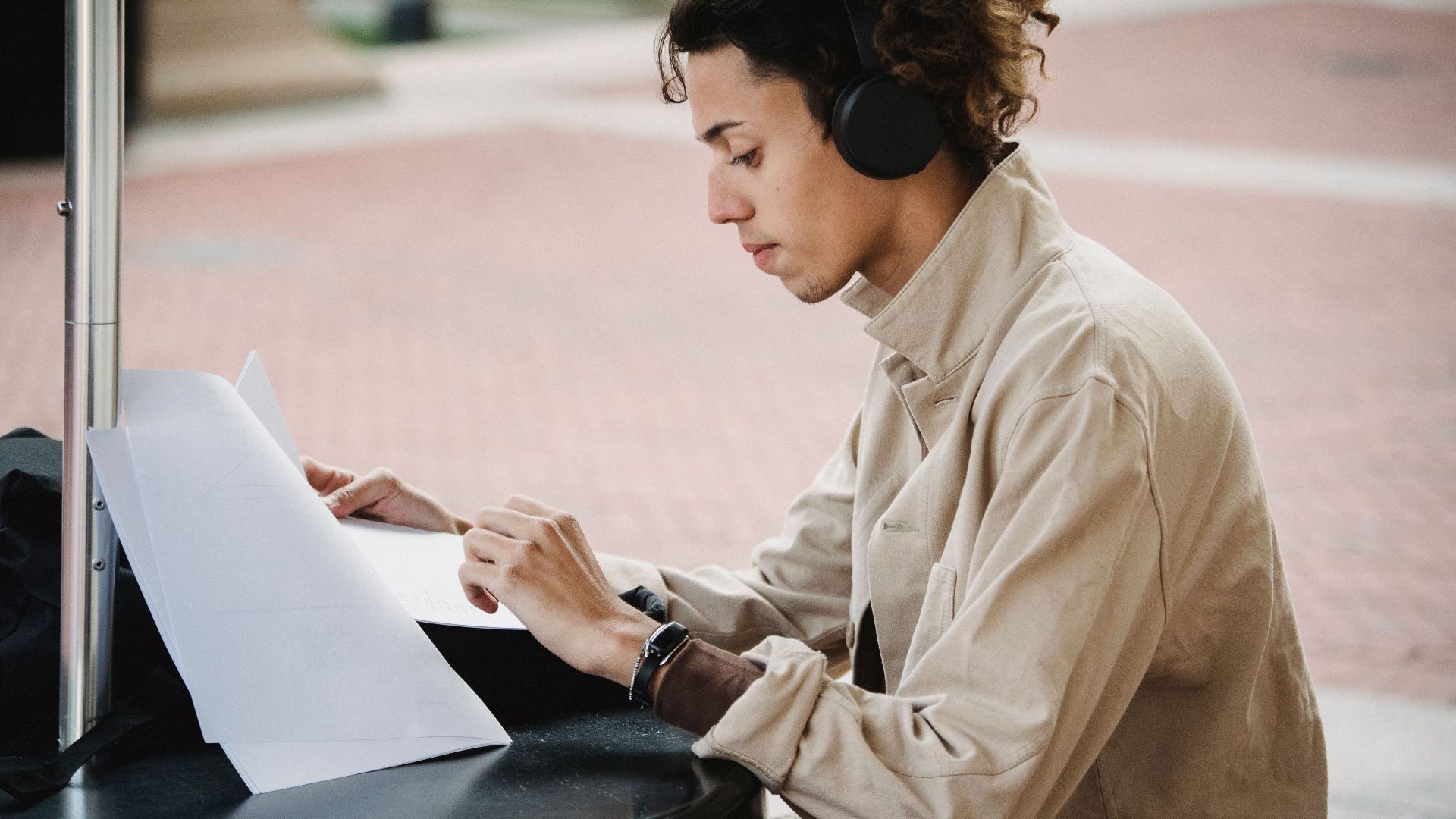 Side view of concentrated male learner preparing report for university assignment while listening to music in wireless headphones