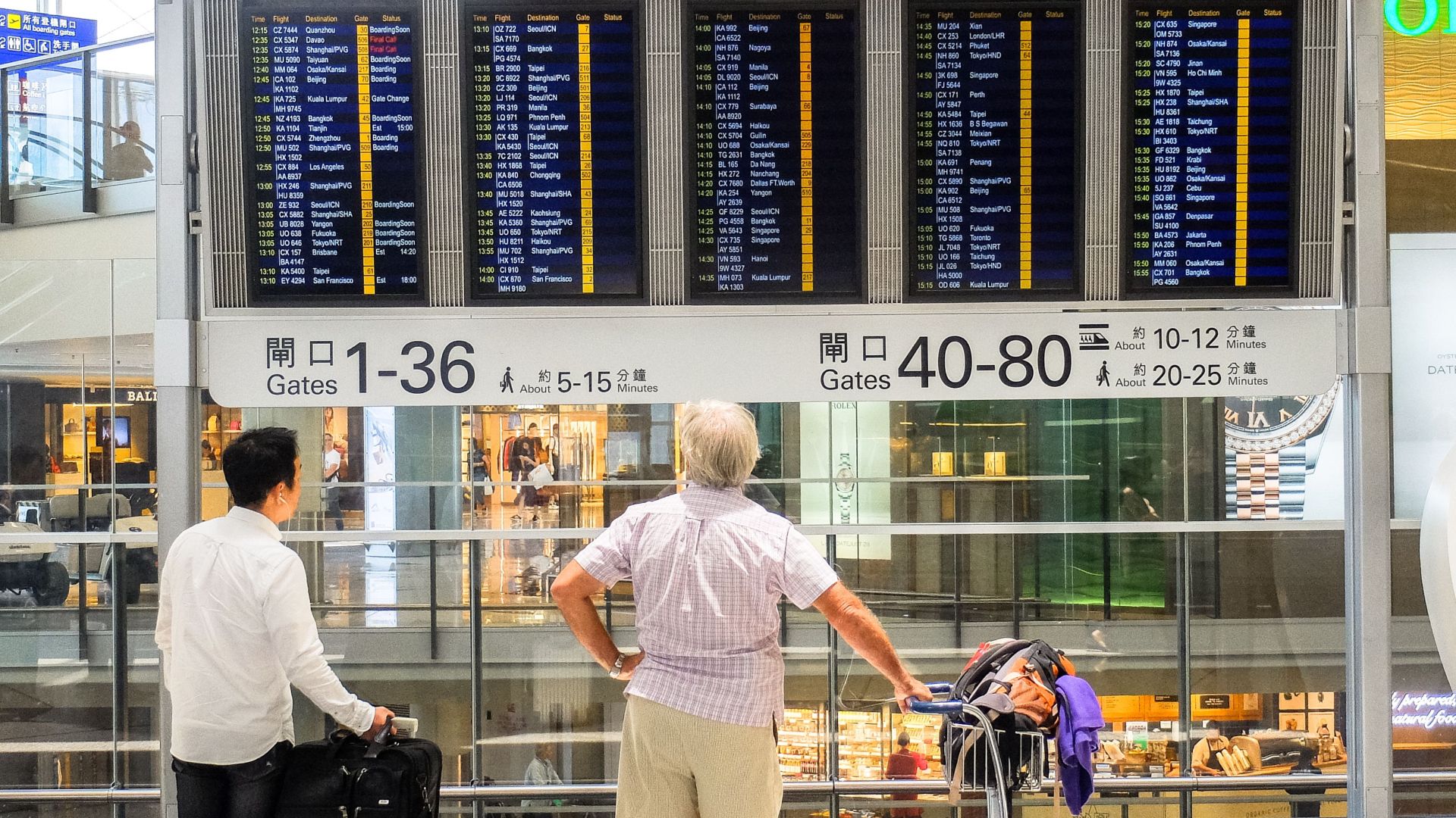 Passengers review flight information on a digital board in Hong Kong airport terminal.