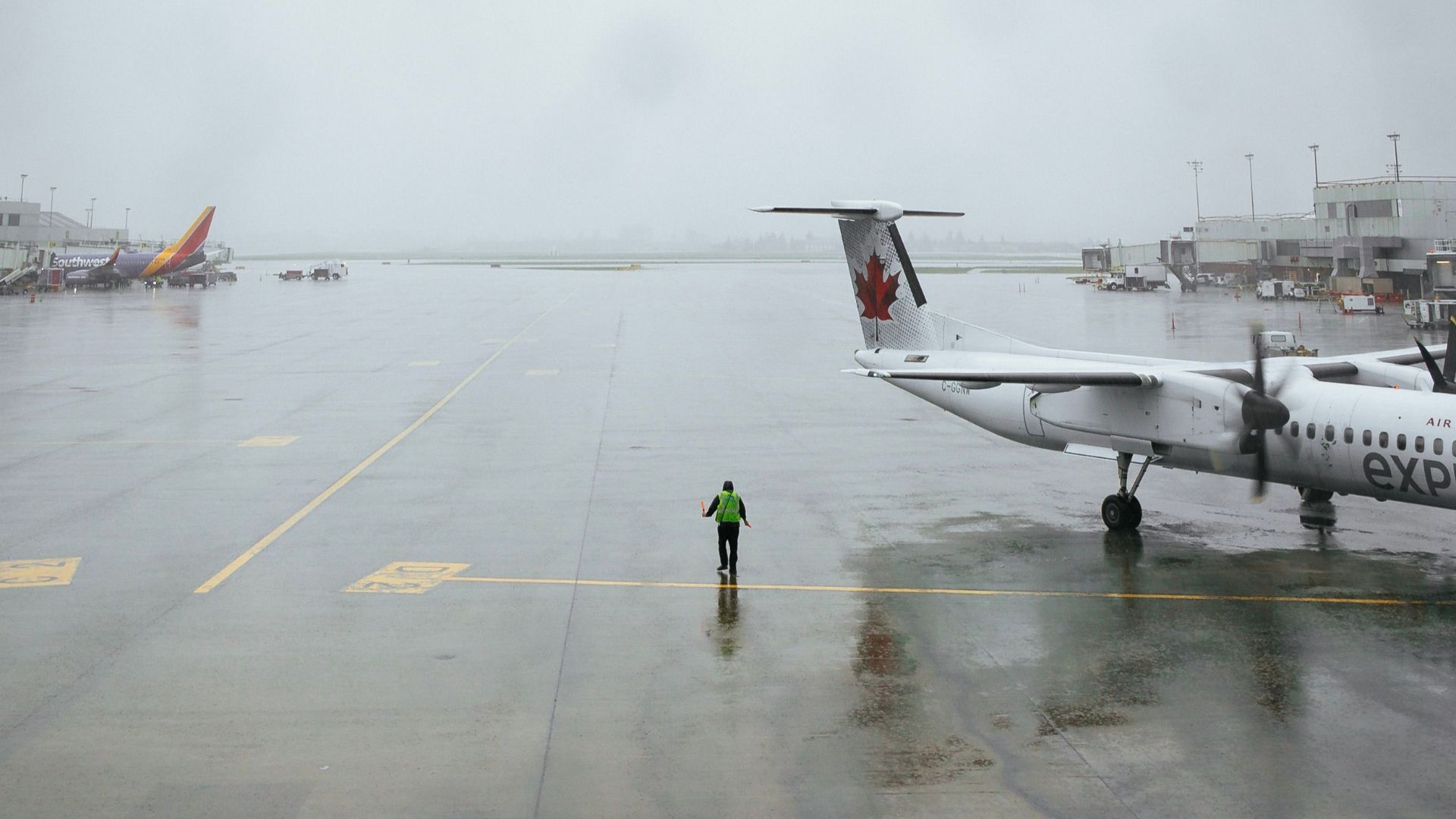 A lone worker on a rainy tarmac with planes at Portland Airport showcases the moody atmosphere.