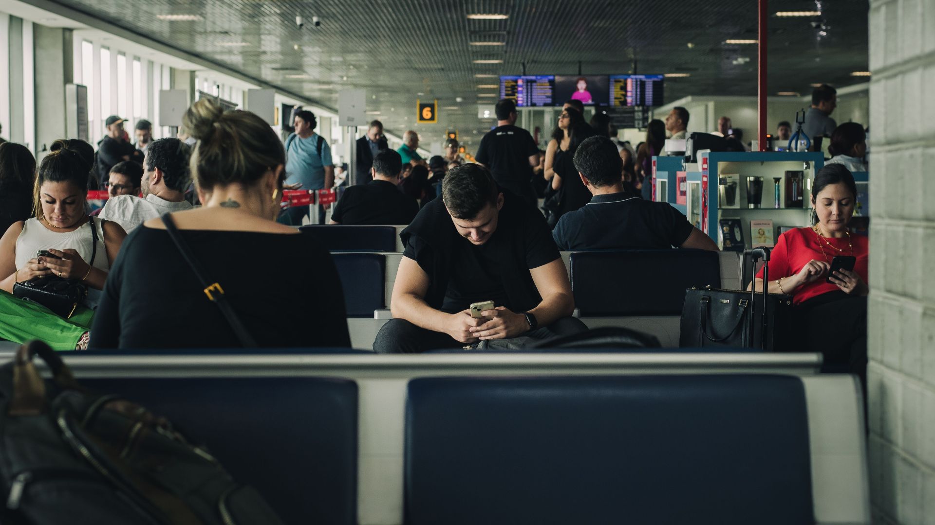 Travelers seated and waiting at São Paulo airport terminal, engaging with smartphones.
