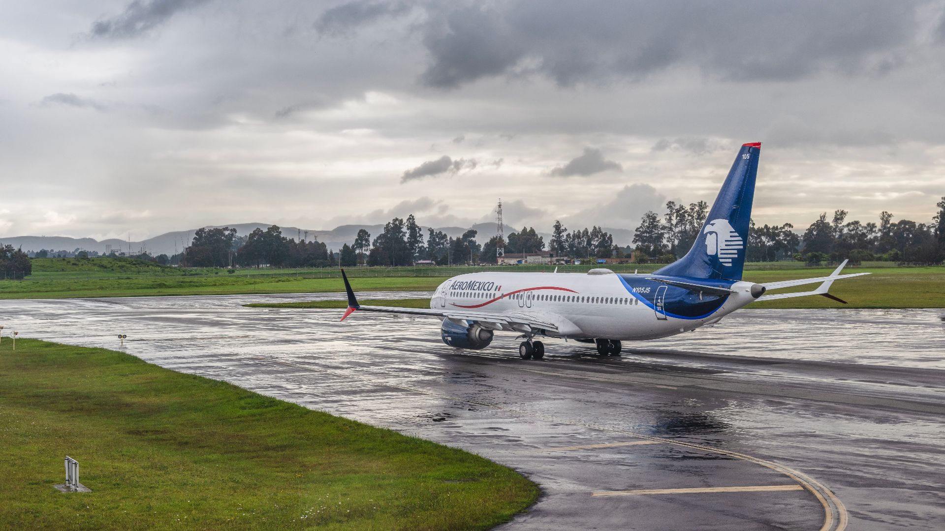 A commercial airplane taxiing on a wet runway under a cloudy sky at an airport.