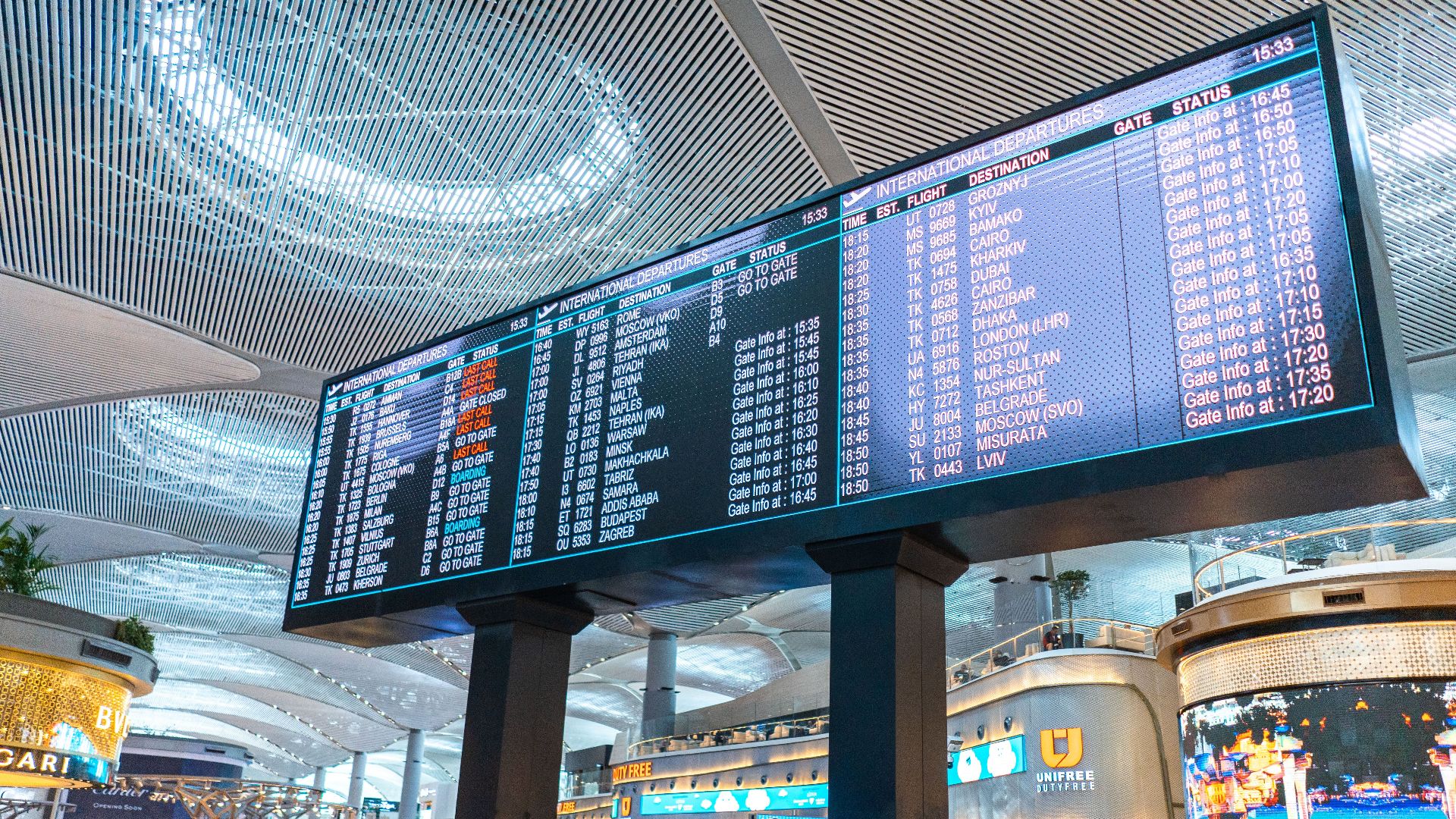 Passengers walk through Istanbul Airport's departure area, surrounded by stores and flight information displays.