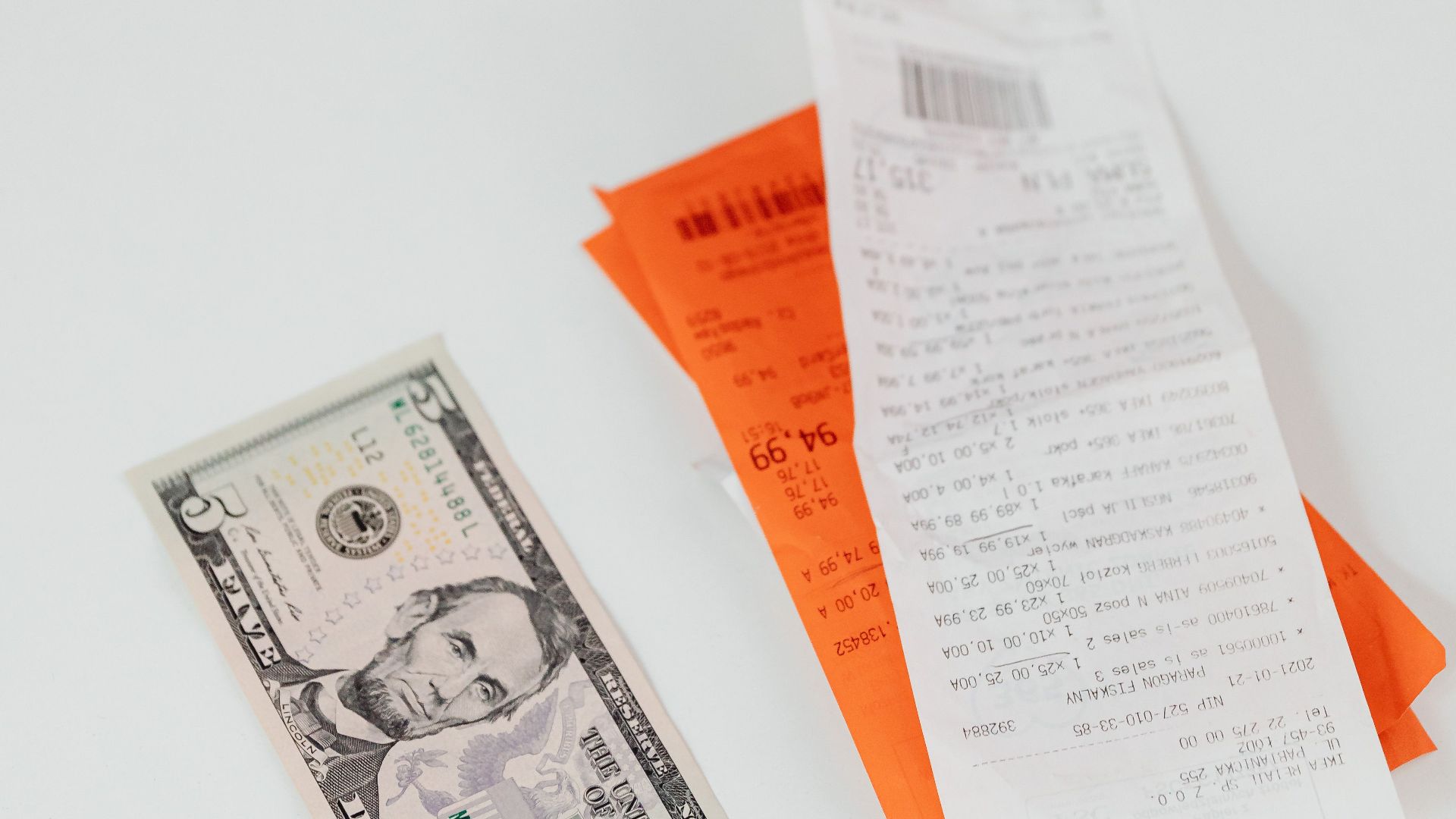 A crisp US dollar bill next to colorful shopping receipts on a clean white surface.
