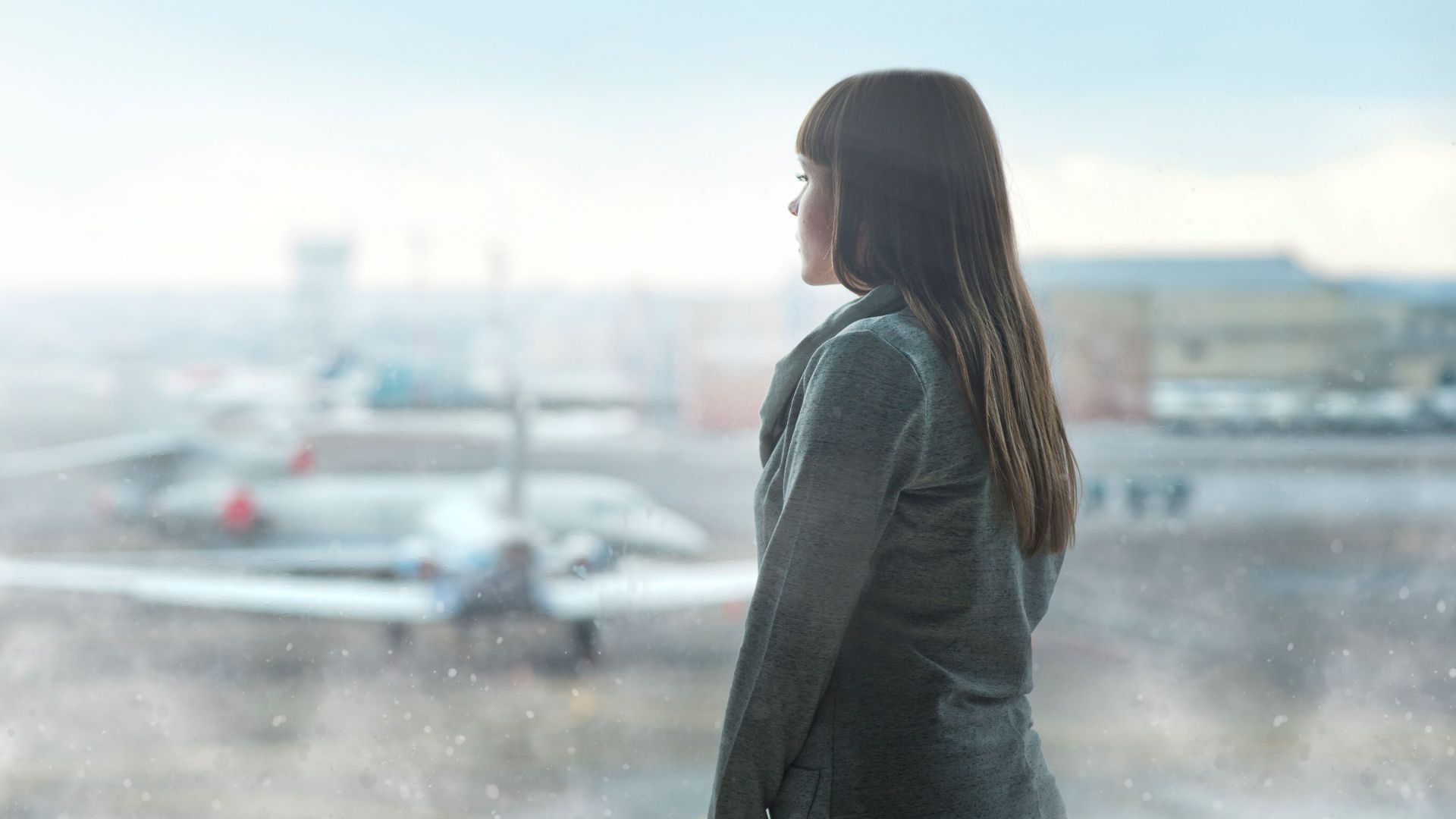 A woman gazing at airplanes through a window at Kyiv's airport terminal, capturing a moment of reflection.
