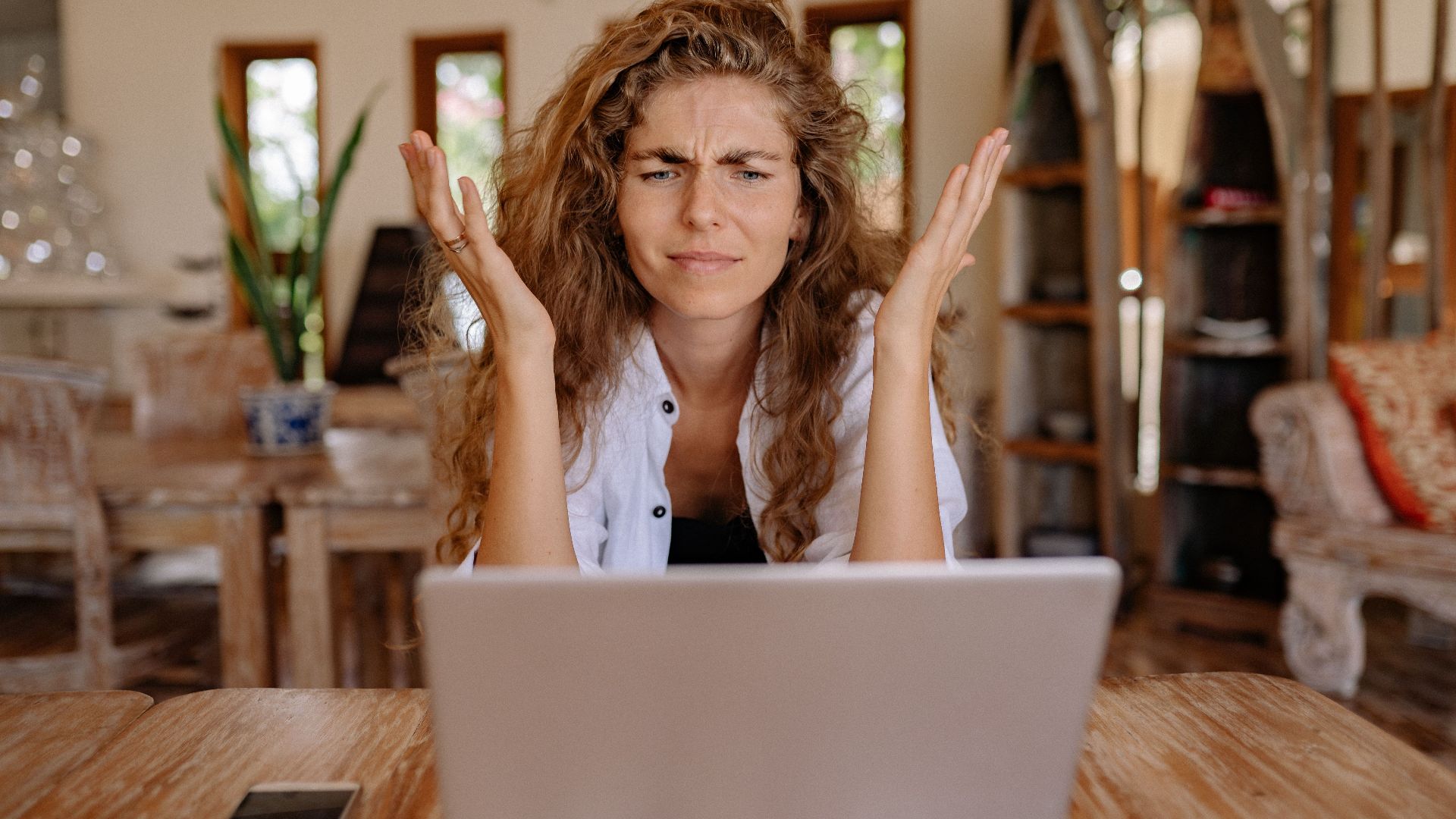 A woman frustrated with her laptop while working remotely indoors, expressing stress.