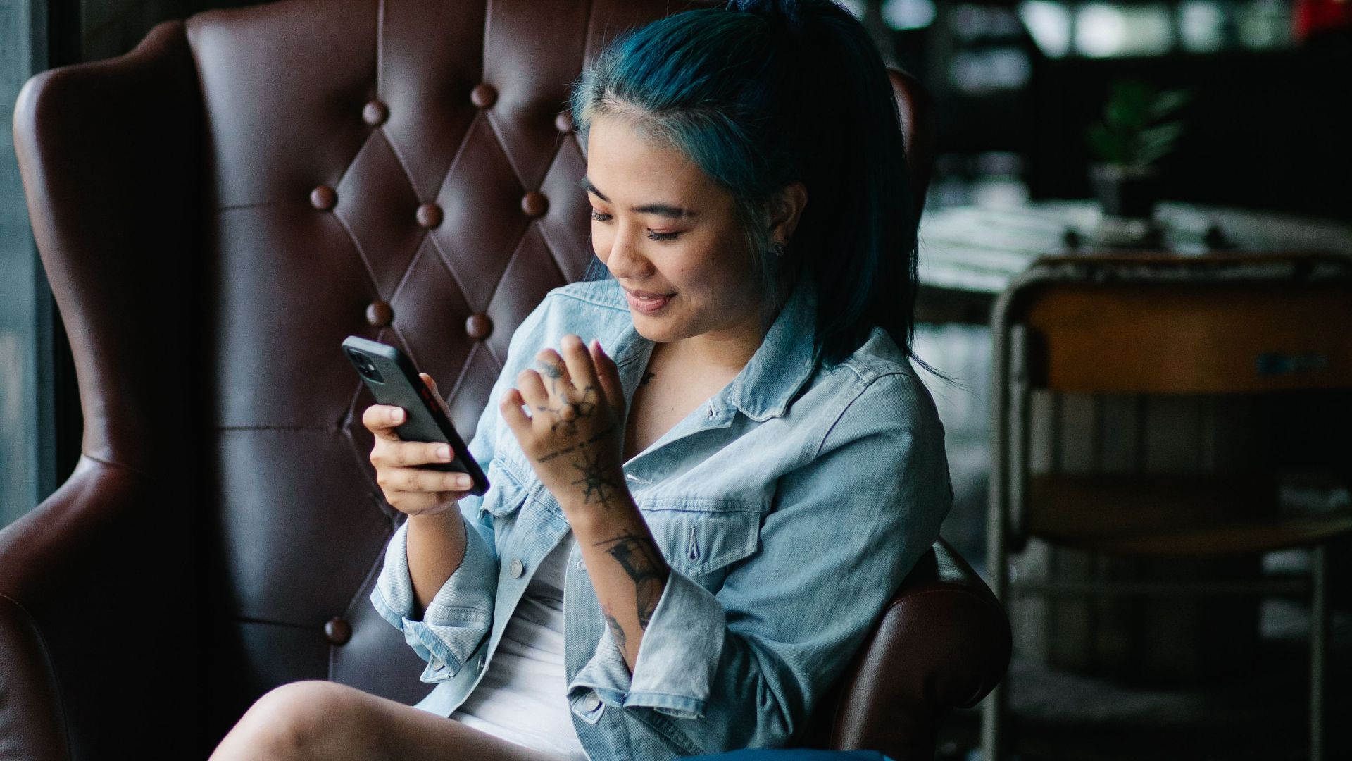 A smiling young woman using her smartphone while sitting in a cozy cafe with a drink nearby.