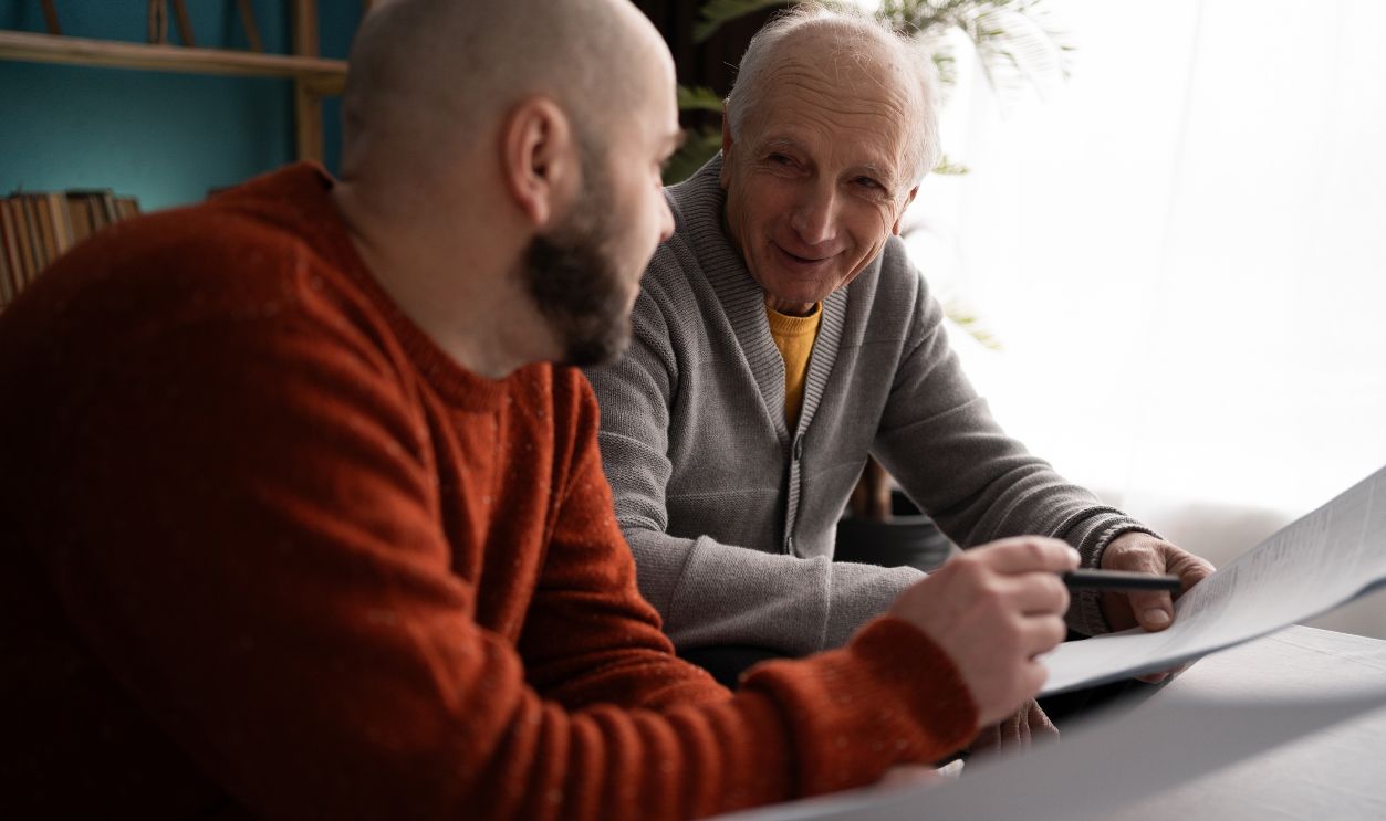 Shutterstock-2579191521, family, care and support concept - adult son assisting elderly father with documents and budget planning at home, reviewing paperwork together