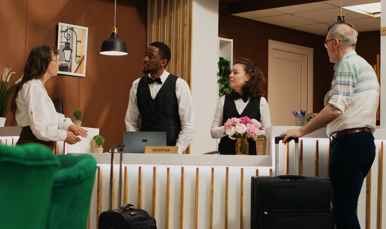 After check in verification, retired people receive room access with key card at hotel. Diverse employees assisting older couple with luggage, providing luxurious concierge services. Handheld shot.