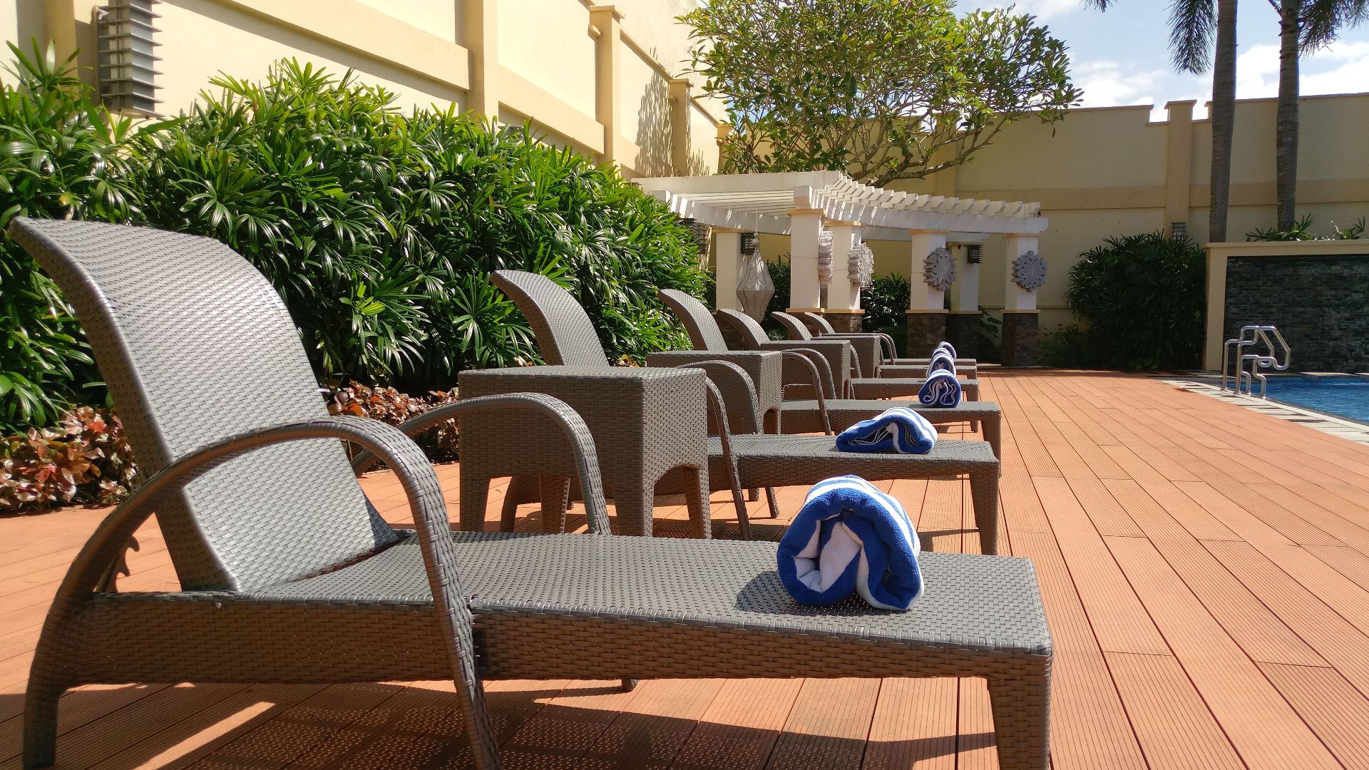 Relax by the pool with elegant lounge chairs and vibrant blue towels under clear skies.