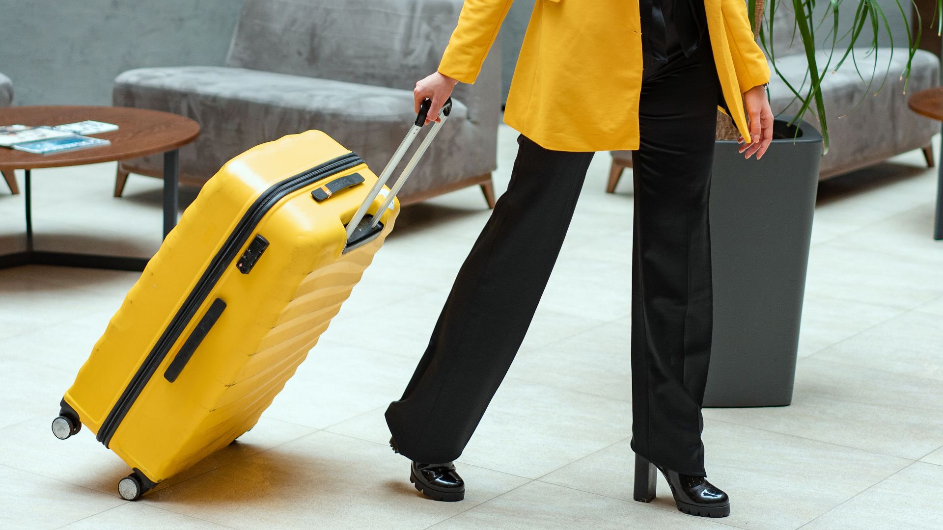 Stylish woman walking in hotel lobby pulling a bright yellow suitcase.