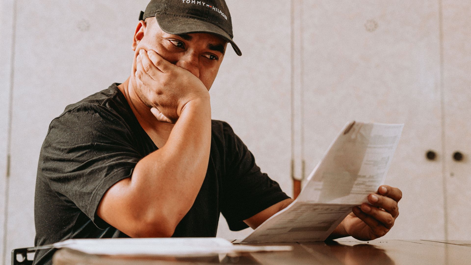 A man sits indoors, deeply focused on reviewing paperwork, expressing concern and contemplation.