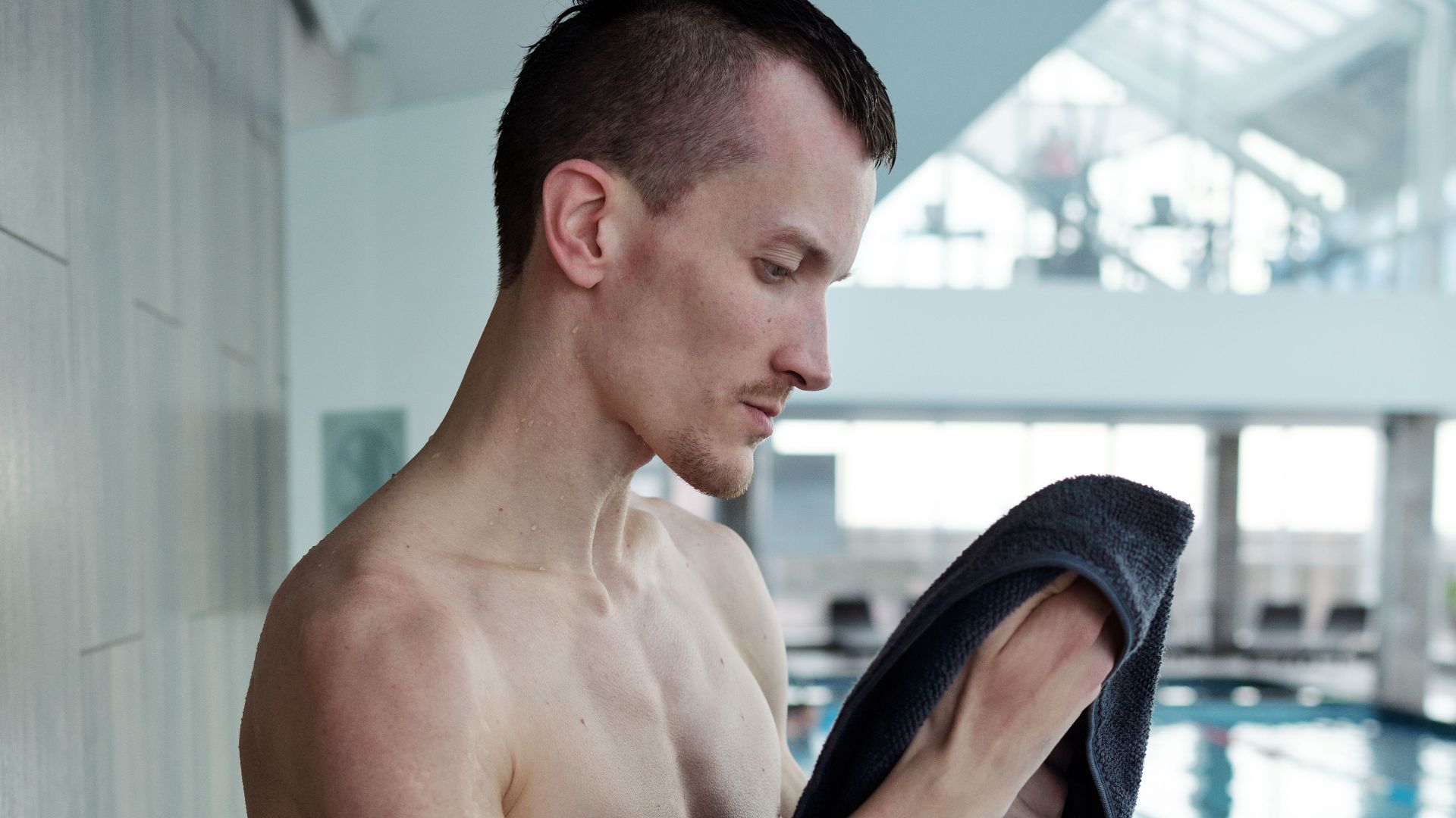 Young amputee man drying off by an indoor swimming pool, representing resilience and determination.
