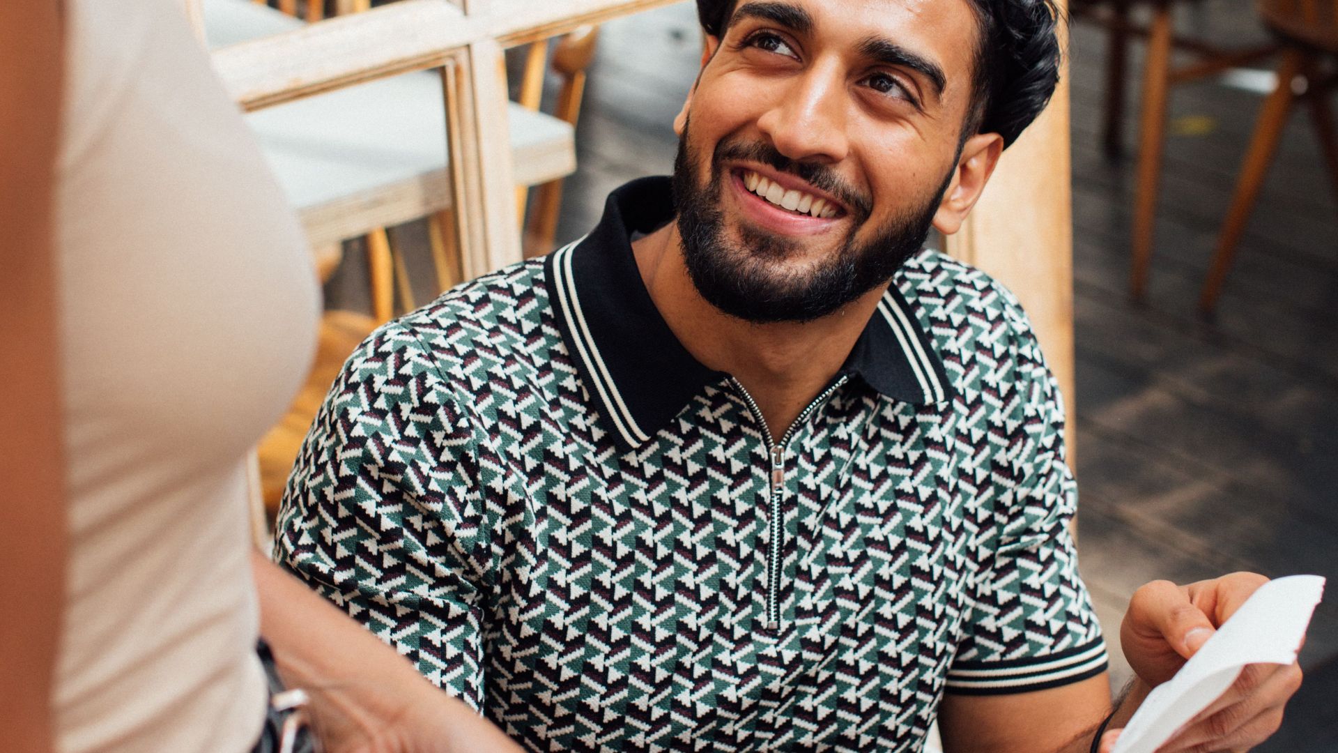 Man smiles while making a contactless payment in a cozy cafe setting.
