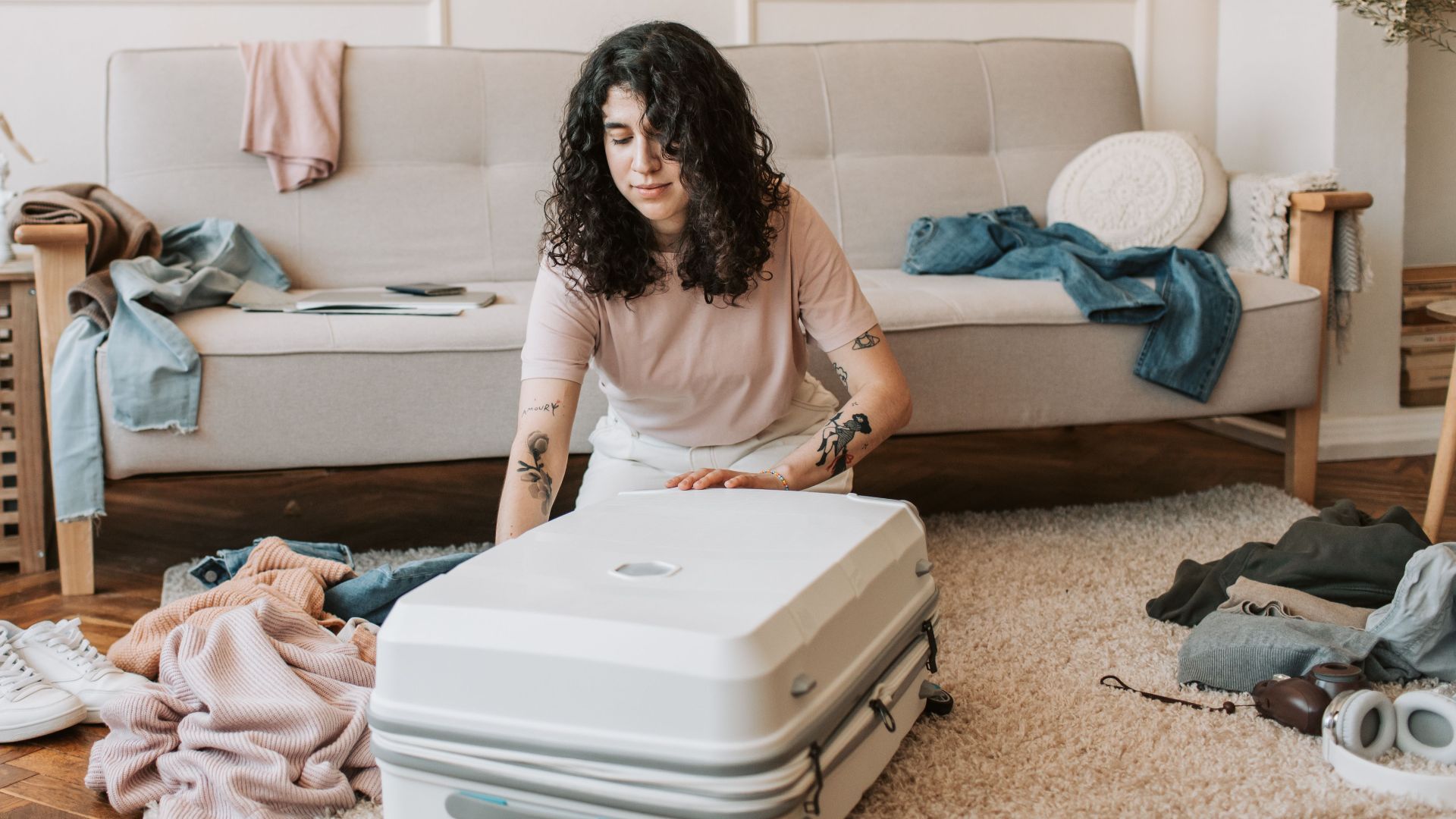 Woman with curly hair packing a suitcase in a stylish living room with a modern, cozy vibe.