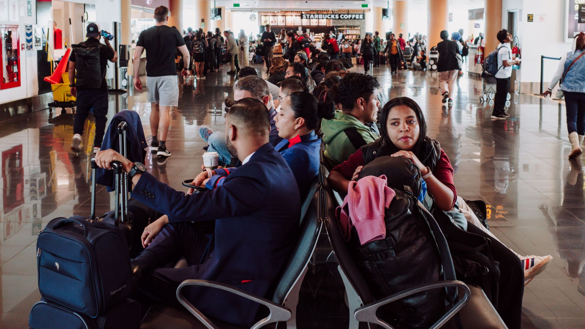 Passengers waiting in a busy airport terminal seating area, with luggage in the modern airport.