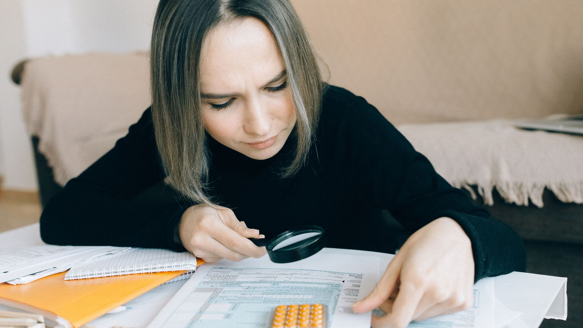 A focused young woman examines documents with a magnifying glass, highlighting attention to detail in accounting tasks.