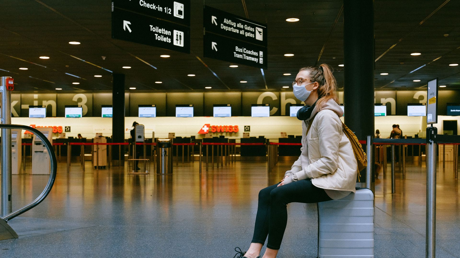 A woman wearing a face mask sits on luggage in an airport terminal amid the pandemic.