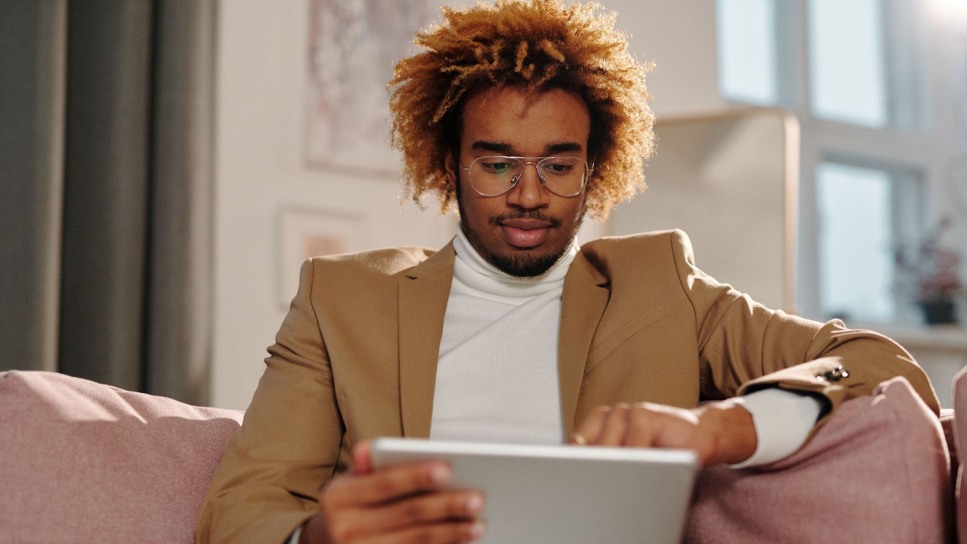 Stylish young man with curly hair using a tablet while relaxing indoors.