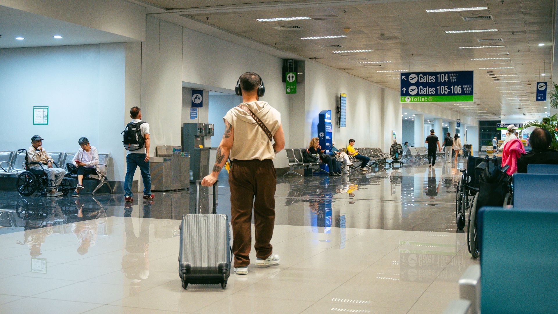 Passengers in a spacious airport terminal, some seated and others walking.