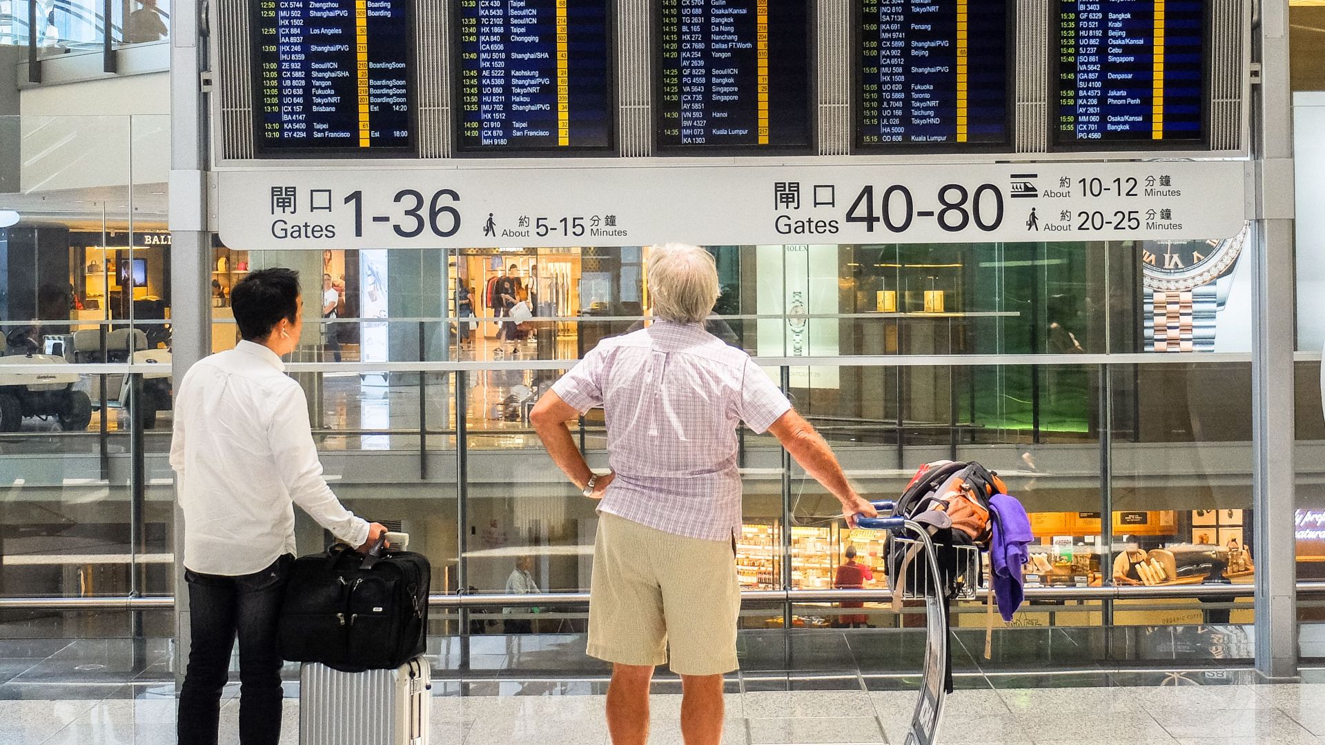 Passengers review flight information on a digital board in Hong Kong airport terminal.
