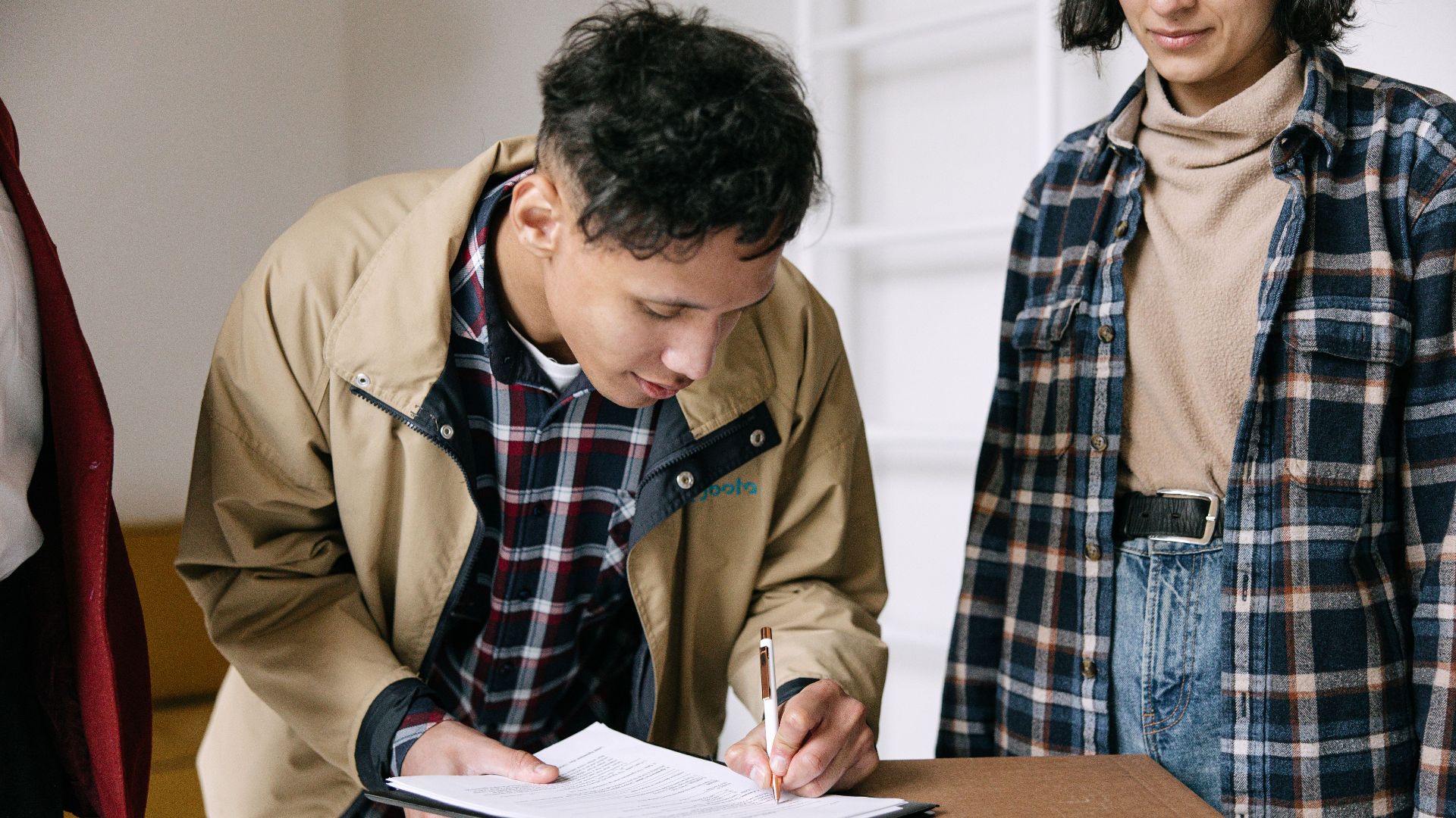 Young adults signing documents on moving day, finalizing new home purchase.
