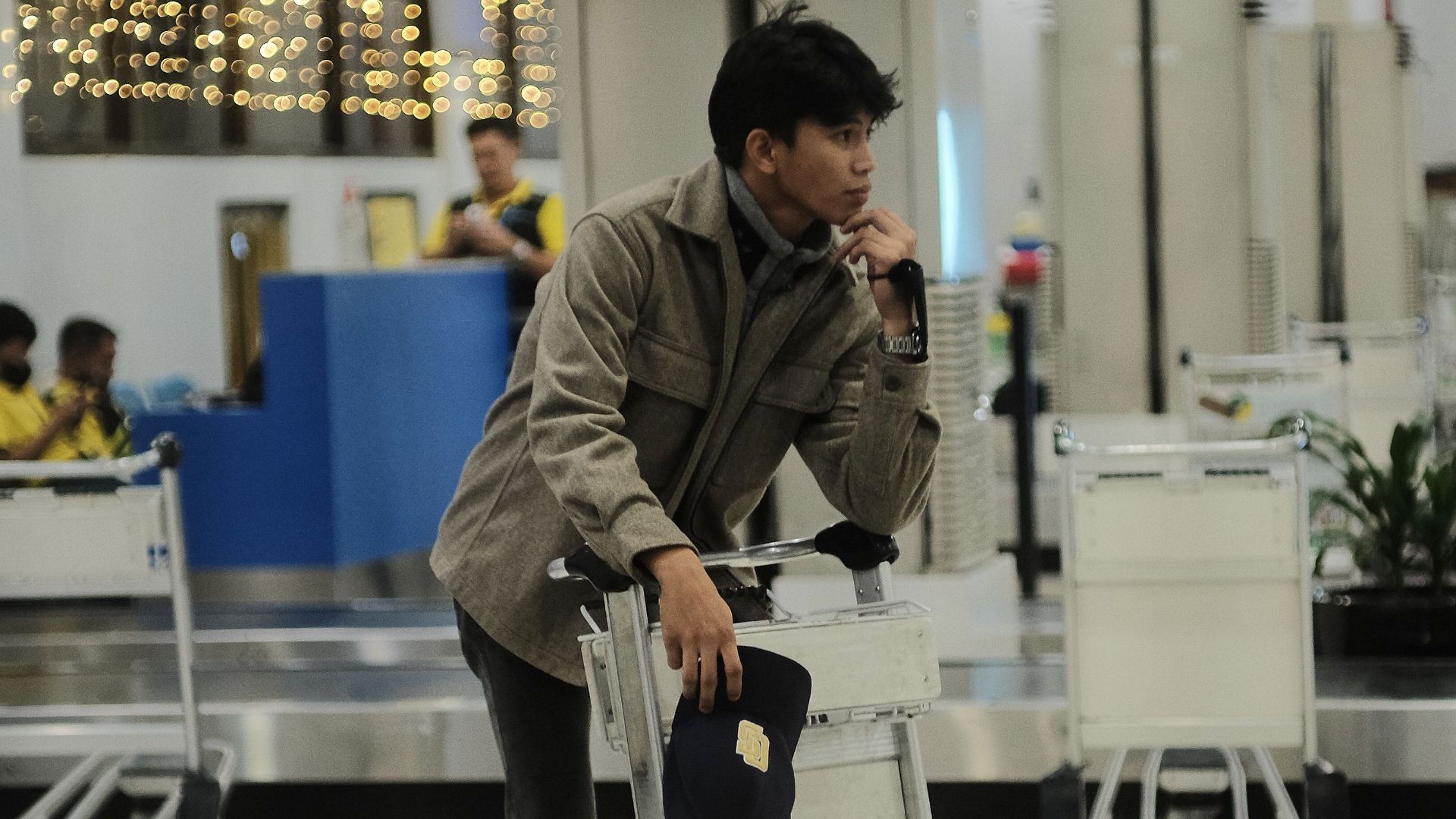 Man in casual attire standing by luggage cart in airport terminal.