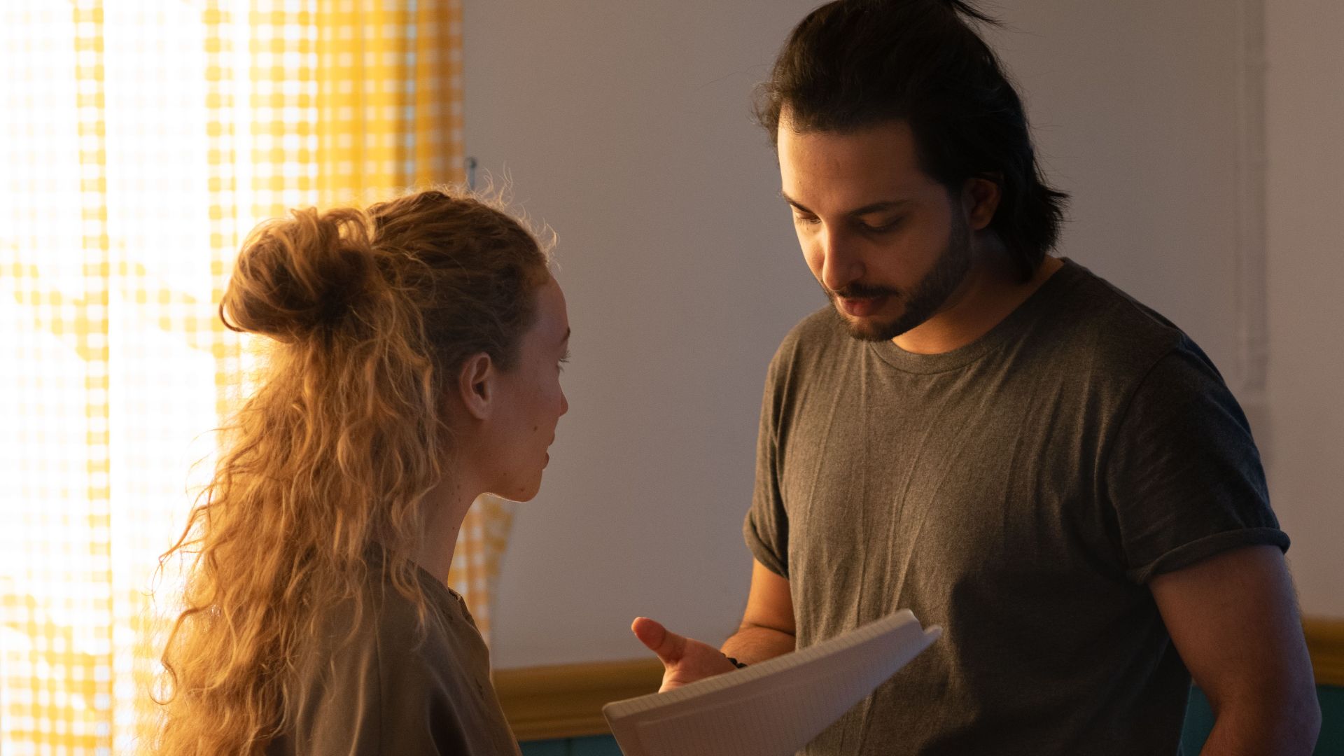 Concentrated couple talking to each other standing in room of new apartment with moved items while woman holding paper sheets and man pointing at paper putting hand in pocket