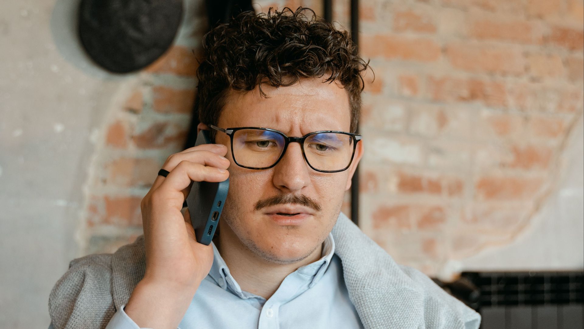 Young man in a casual indoor setting, making a phone call while wearing glasses.