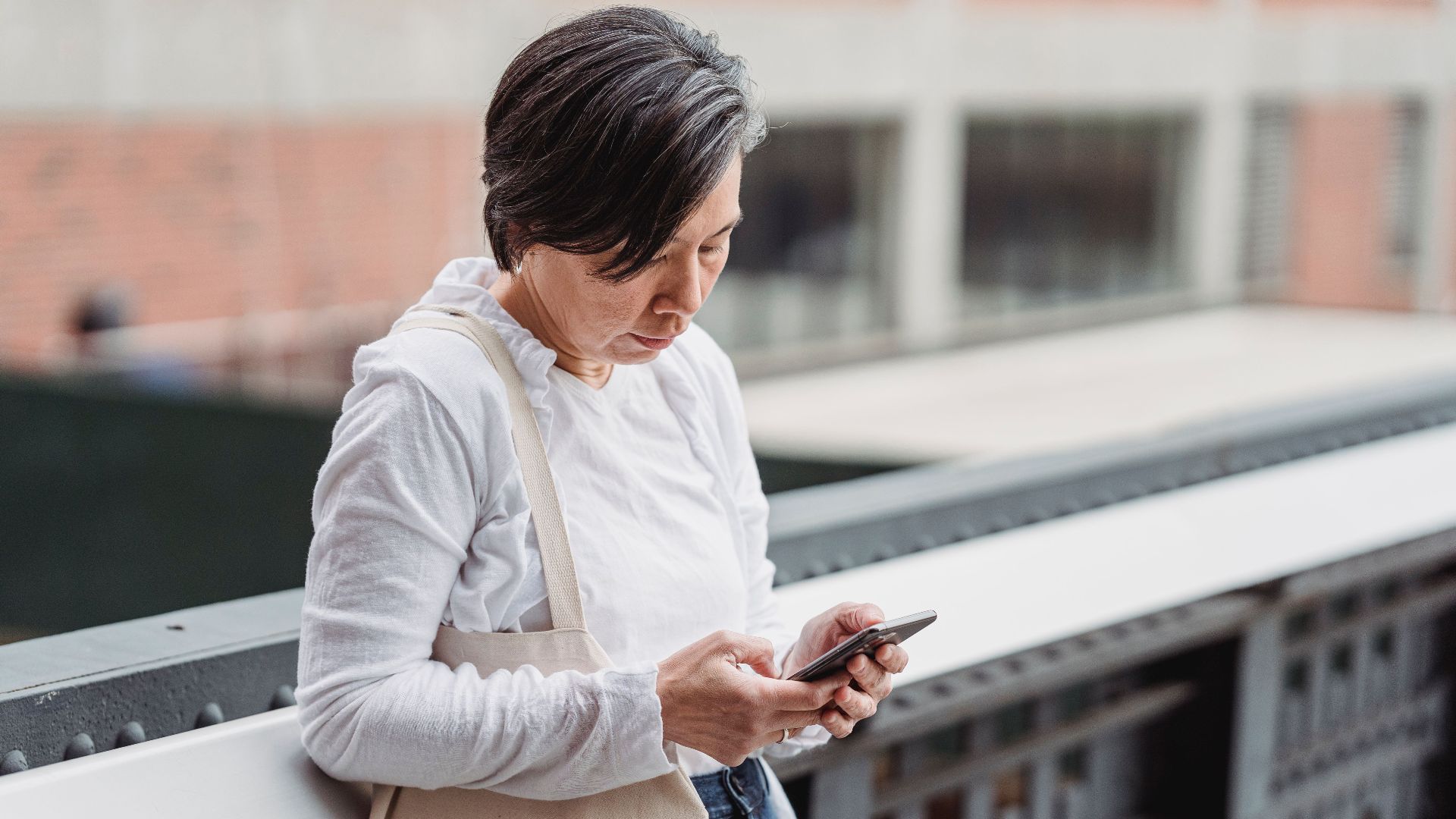 Casual scene of a woman interacting with her smartphone outdoors, leaning on railings.