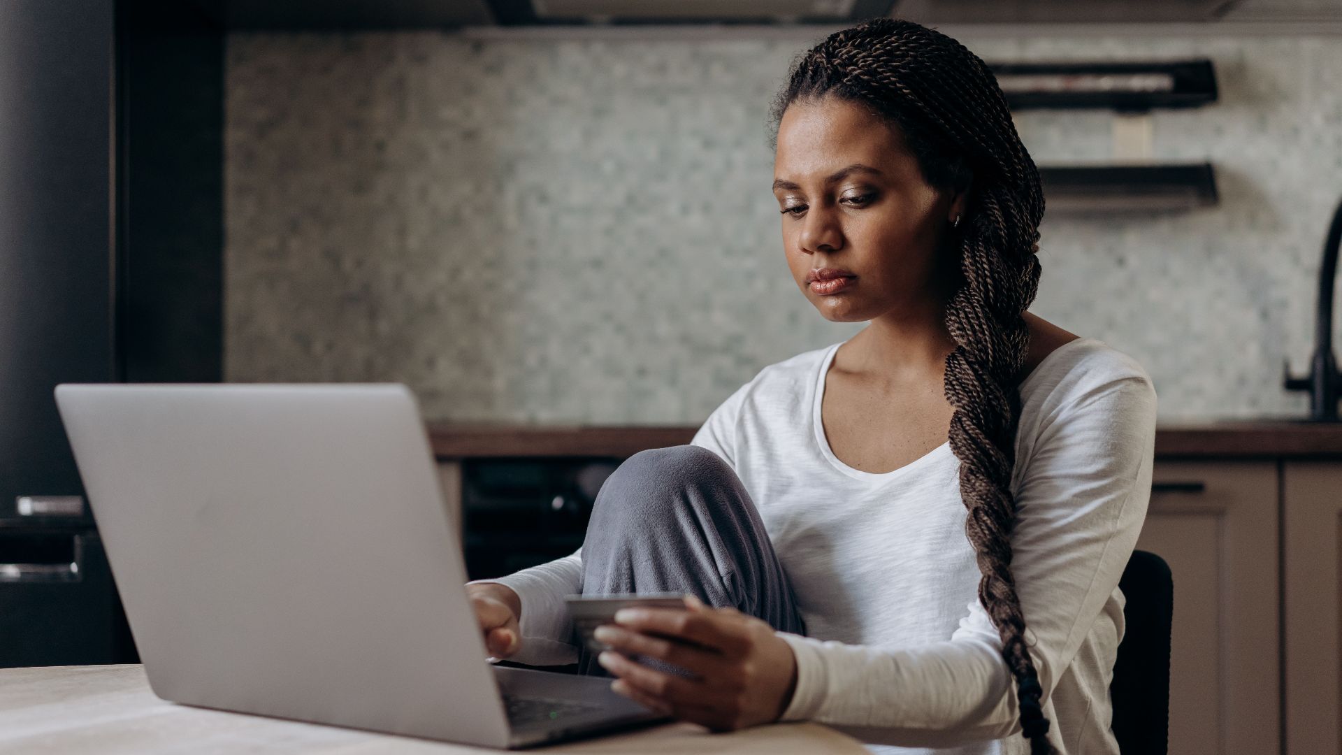 Young woman with braids using laptop and credit card for online shopping indoors.
