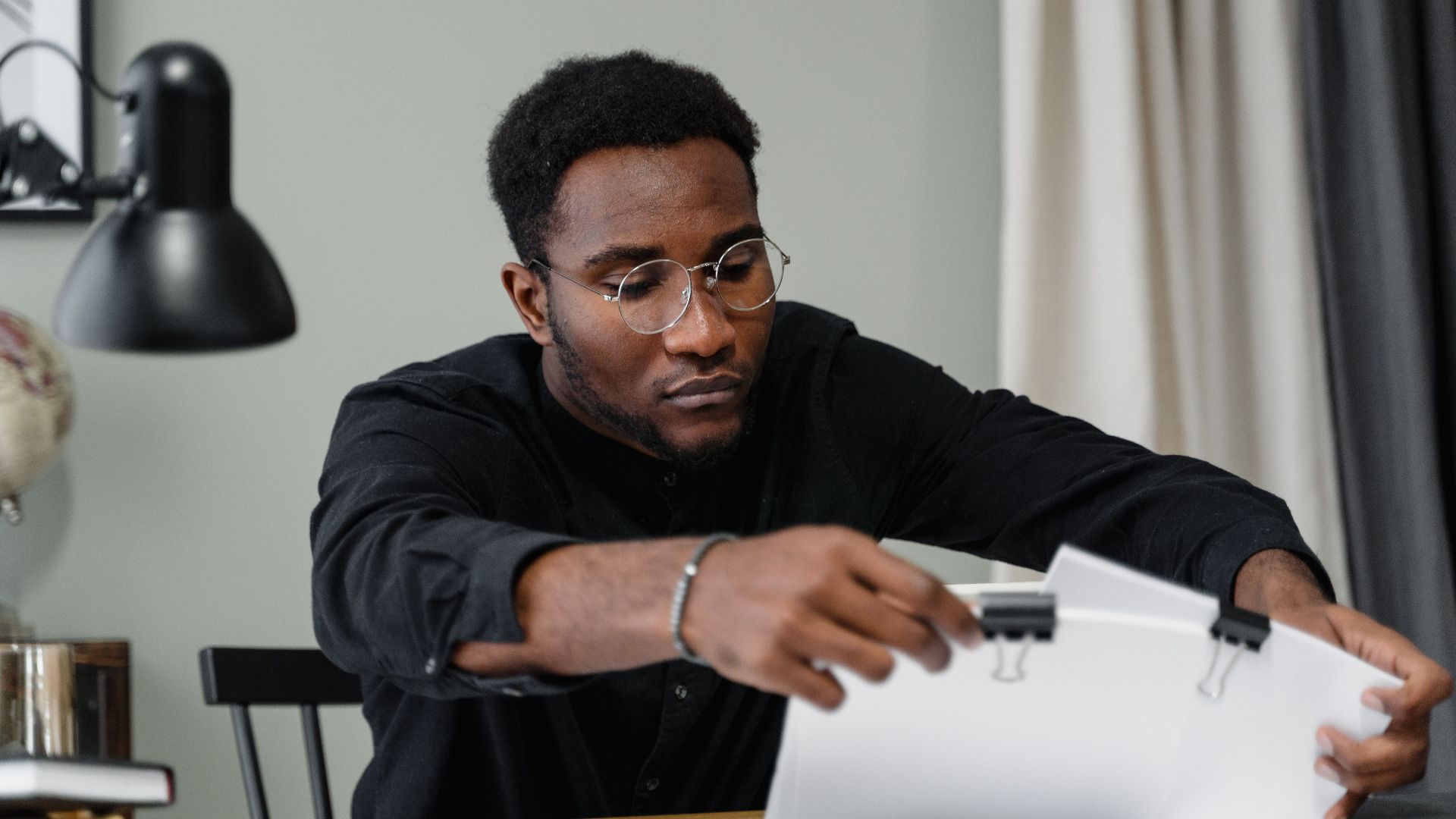 Professional man with glasses reviews documents at a desk in an office setting, emphasizing concentration.