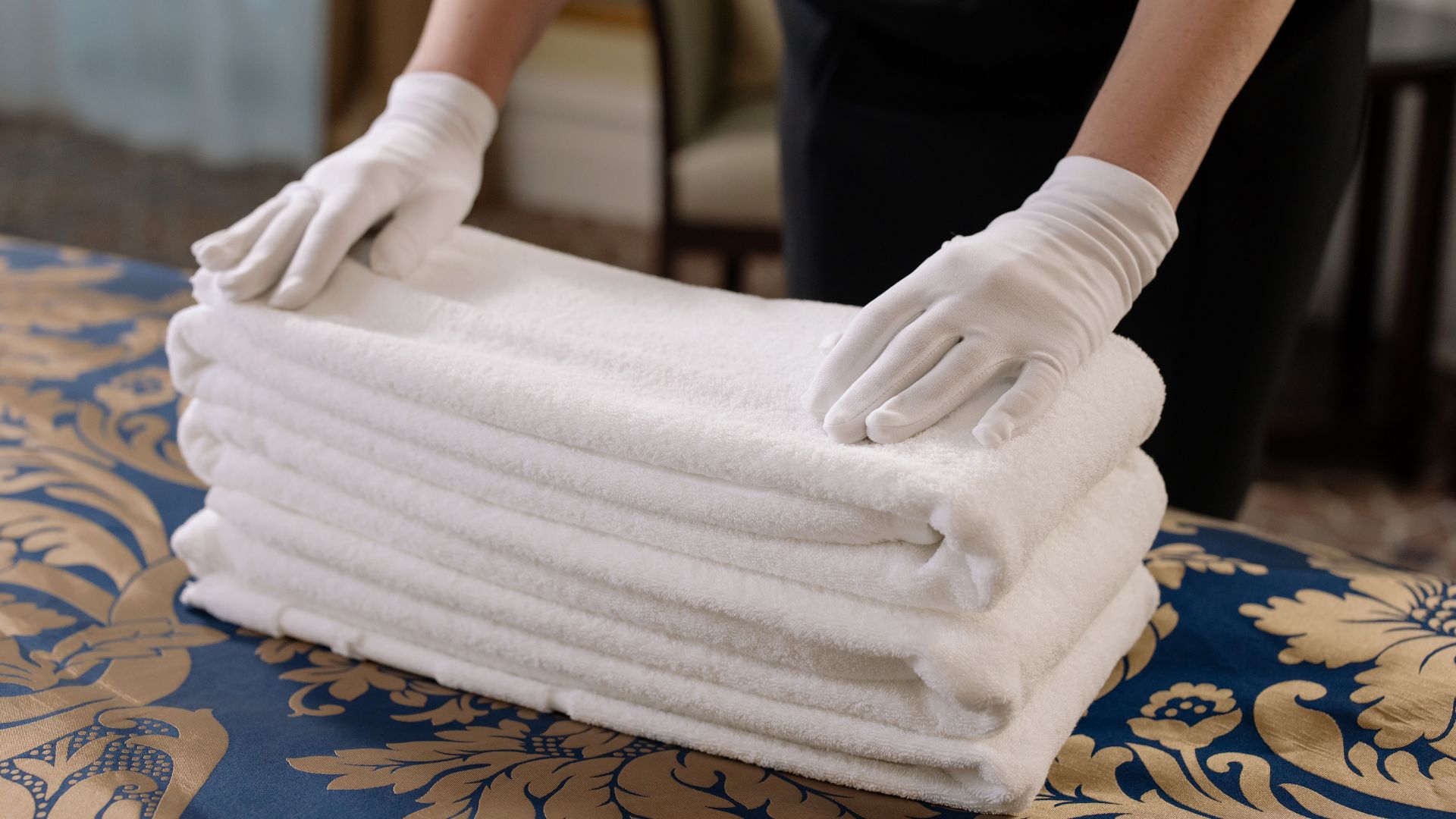 Professional housekeeper folding clean towels on a bed in a hotel room, emphasizing neatness and service.