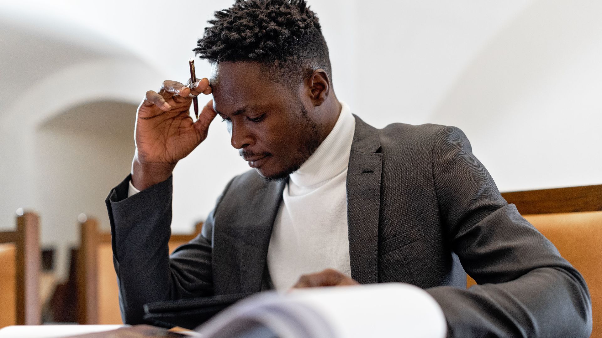 A focused businessman in a suit examines documents while deep in thought in an office setting.