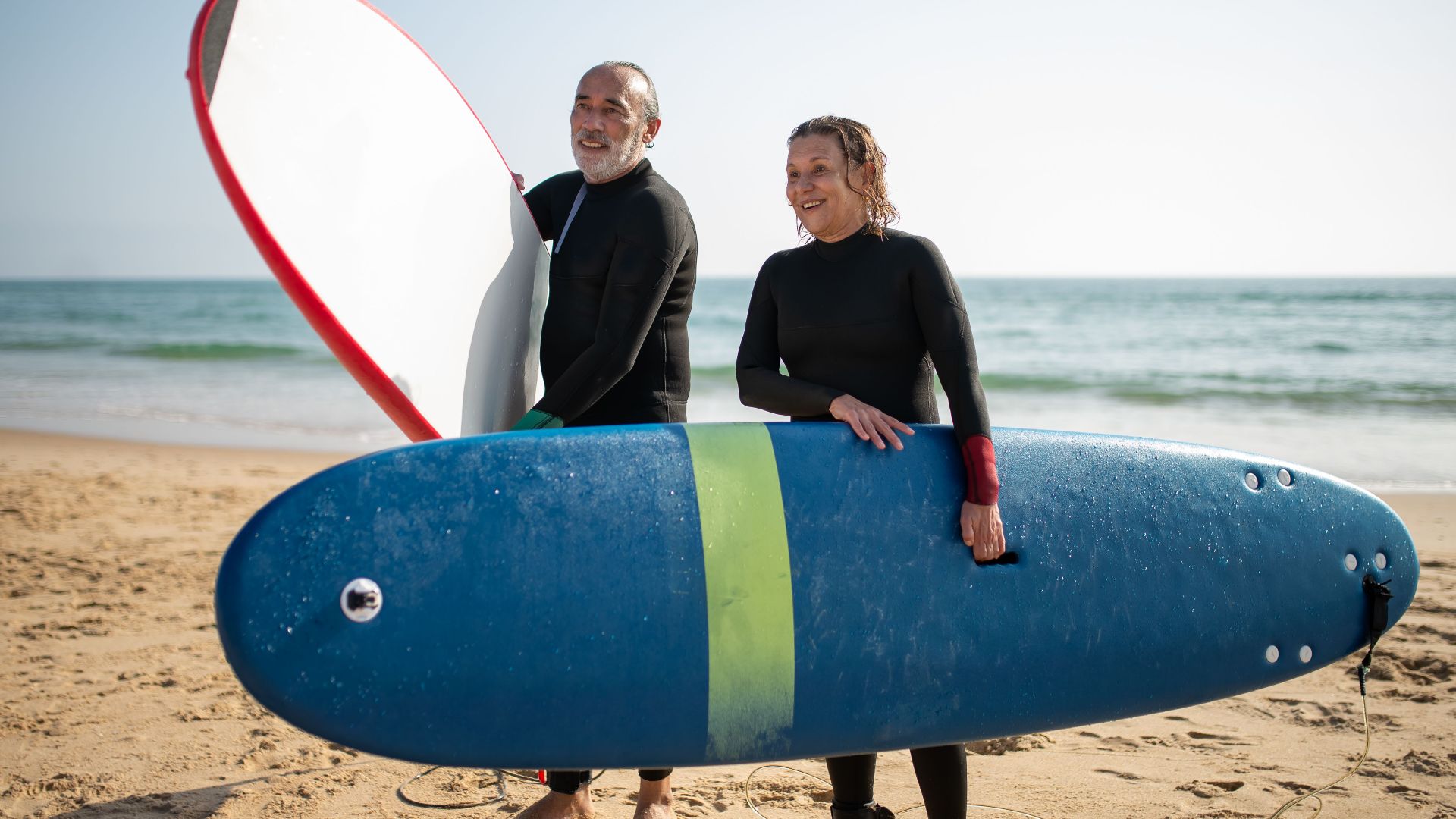 Senior couple enjoying a sunny beach day in Portugal with surfboards.