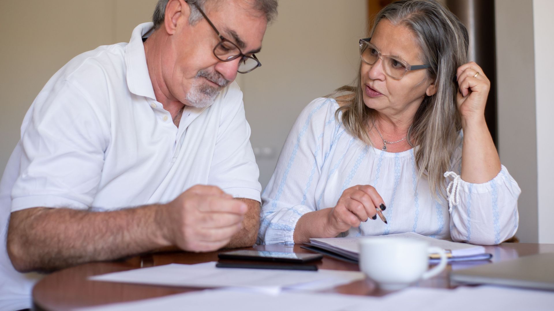 Senior couple reviewing documents and managing finances together at home, showing collaboration and care.