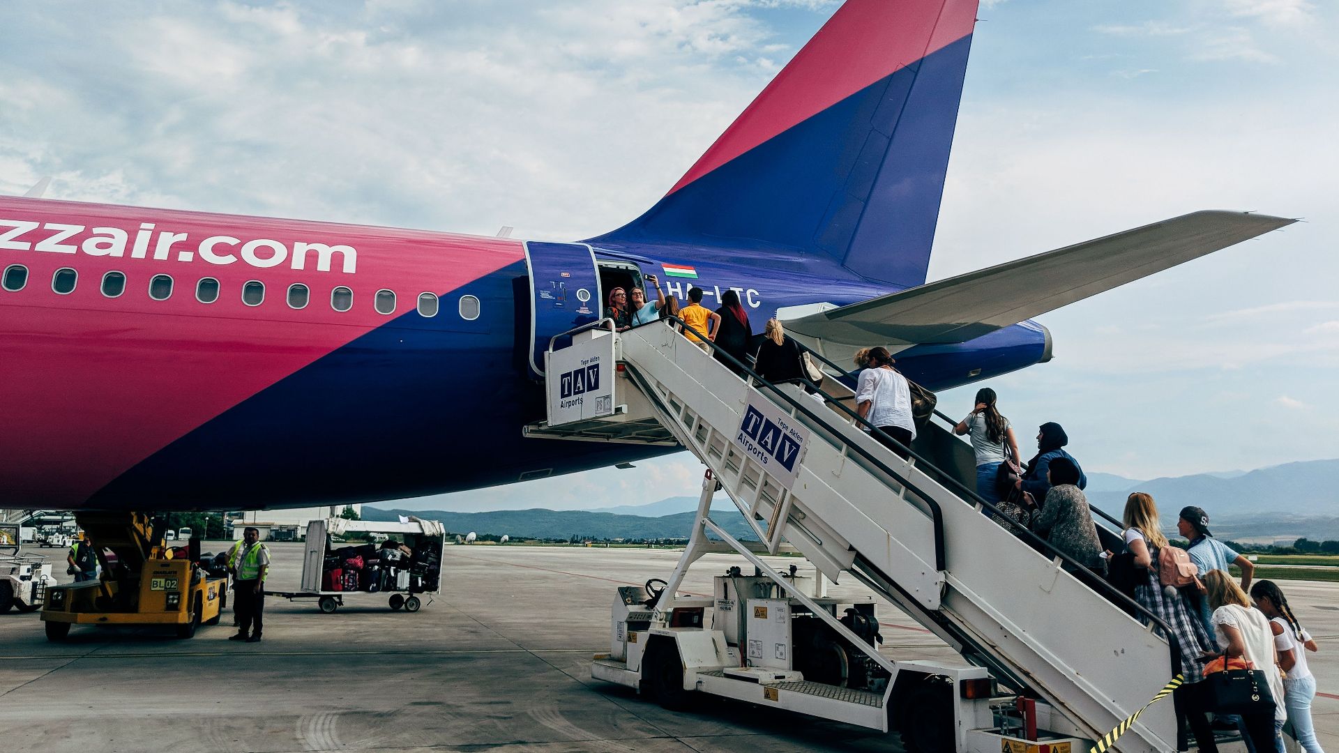Travelers boarding a WizzAir Airbus A320 jet on a clear day at the airport.