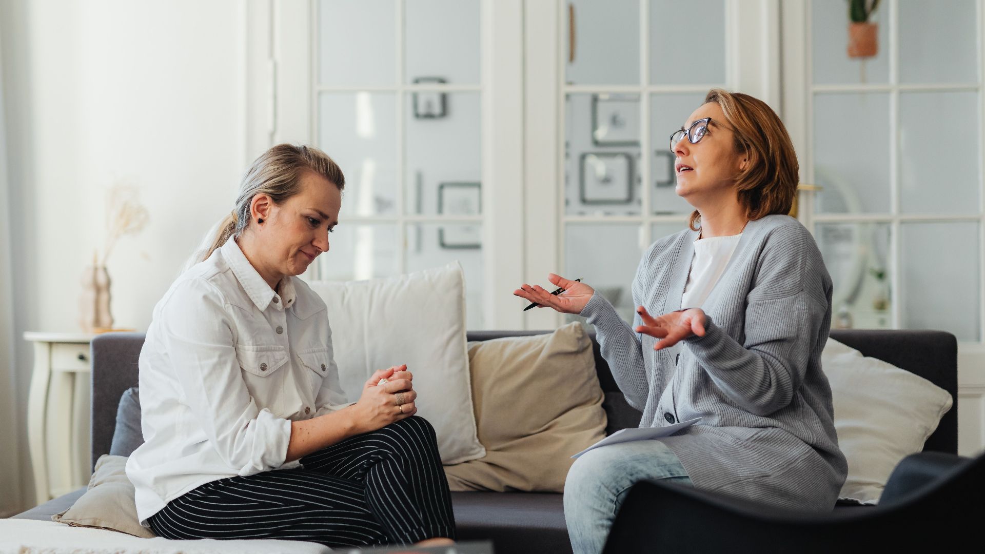 Two women having a conversation in a bright, cozy living room.