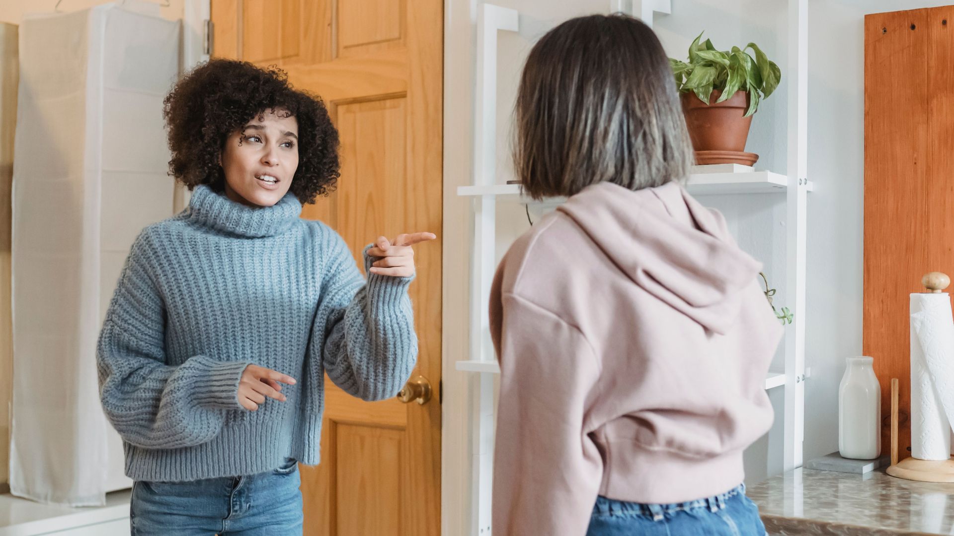 Angry African American female complaining and pointing at faceless female while having fight i modern flat with green plants