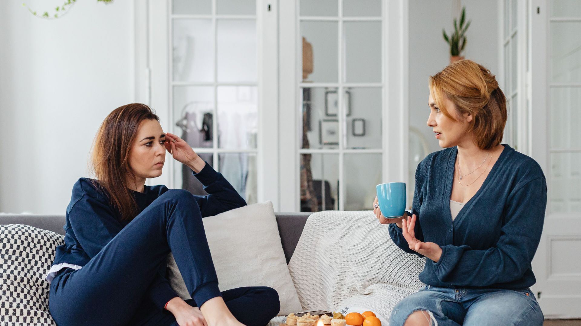 Two women having a heartfelt conversation in a modern living room setting.