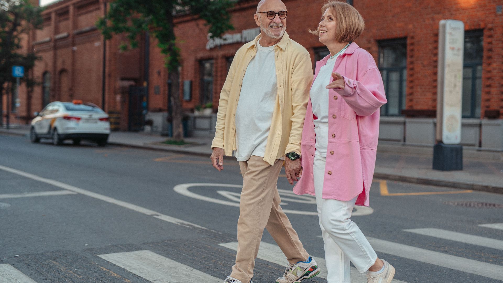 Happy senior couple walking hand in hand across a city pedestrian crossing.