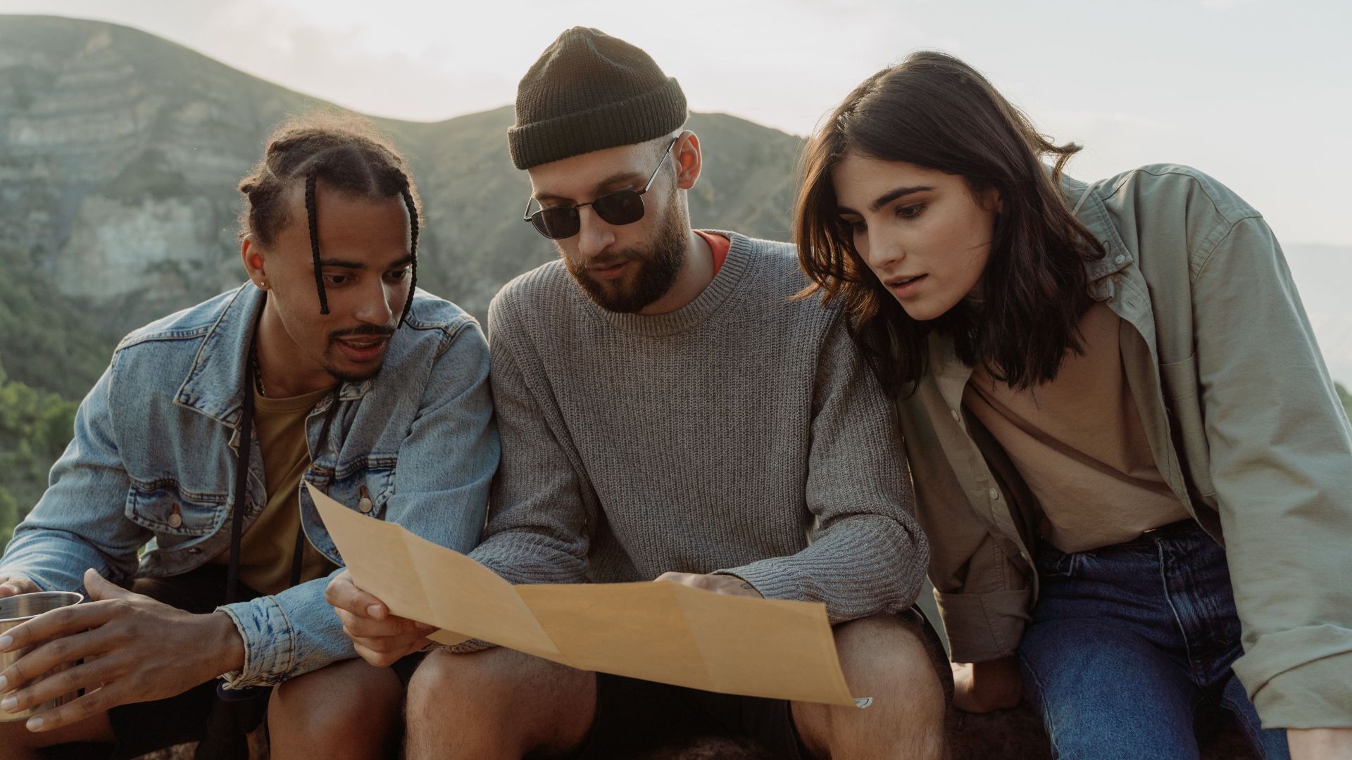 Three young adults studying a map while hiking in the mountains on a sunny day.